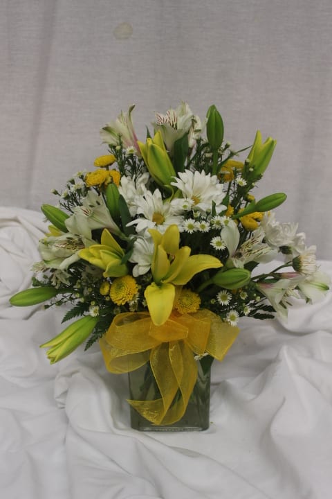 Yellow lilies and white daisies in a glass vase with a yellow ribbon