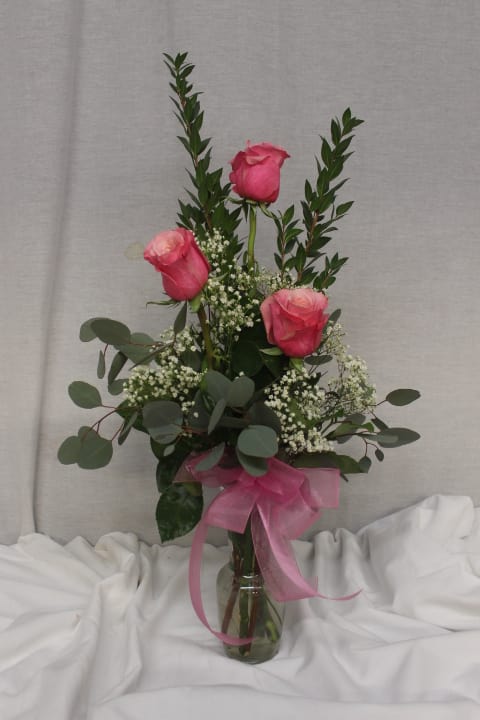 Pink roses in a glass vase with baby's breath and a pink ribbon
