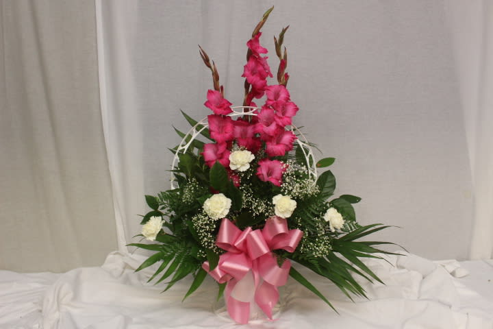 Pink gladiolus arrangement with white carnations in a basket and pink ribbon
