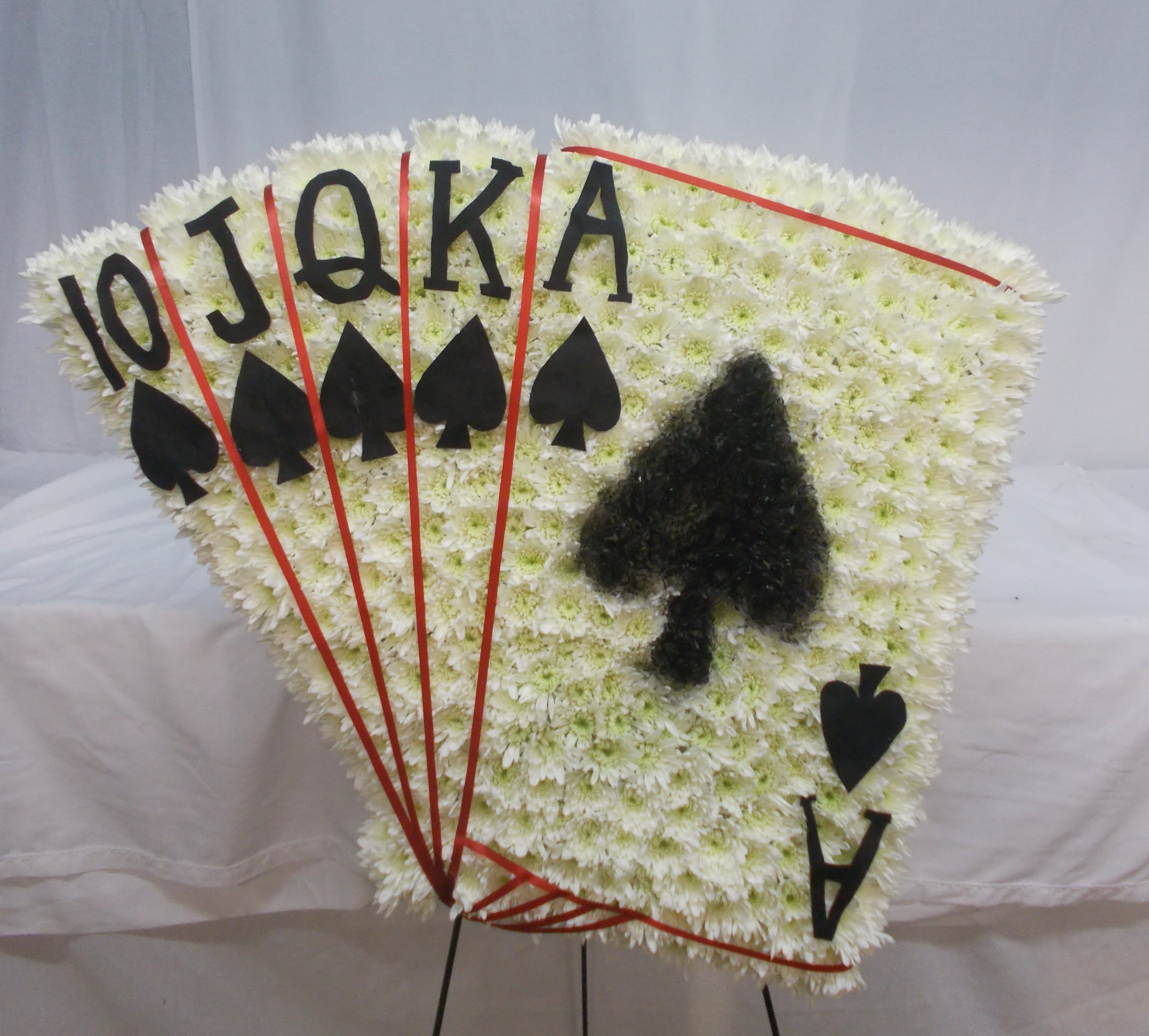 Fan-shaped white floral tribute with playing card symbols and letters