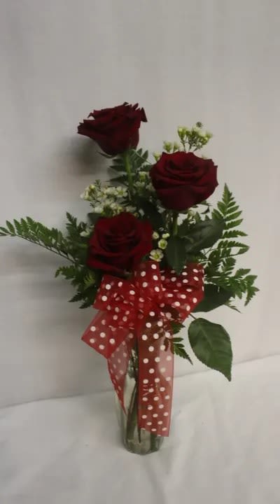 Three red roses in a glass vase with a red polka-dot bow