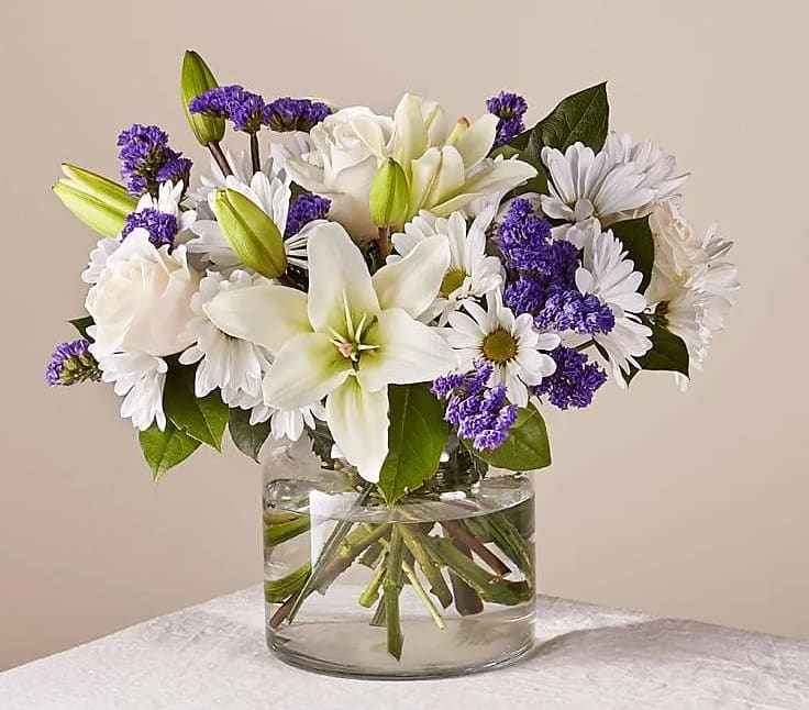 White lilies, roses, and daisies in a clear glass vase
