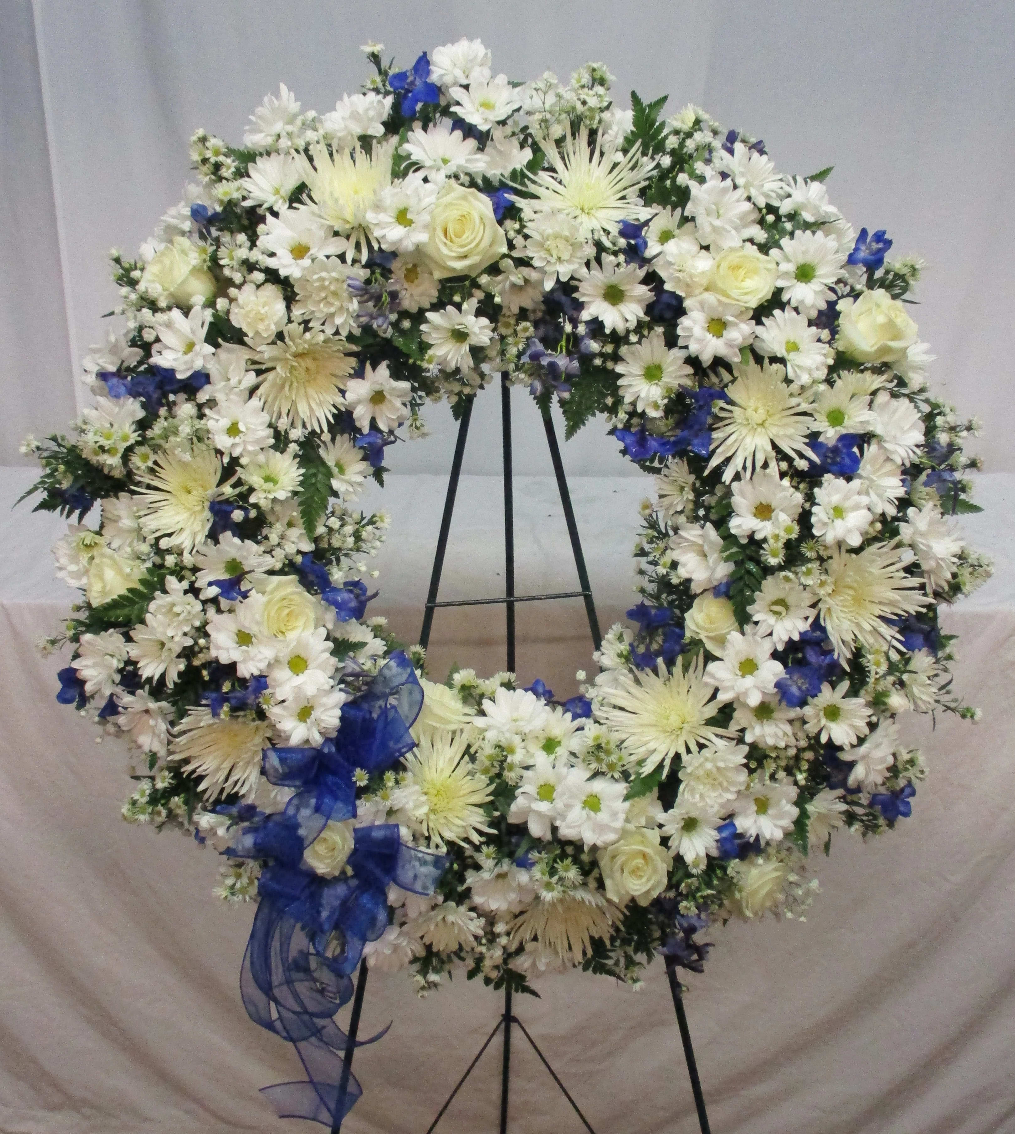 Large white and blue floral wreath on a black stand