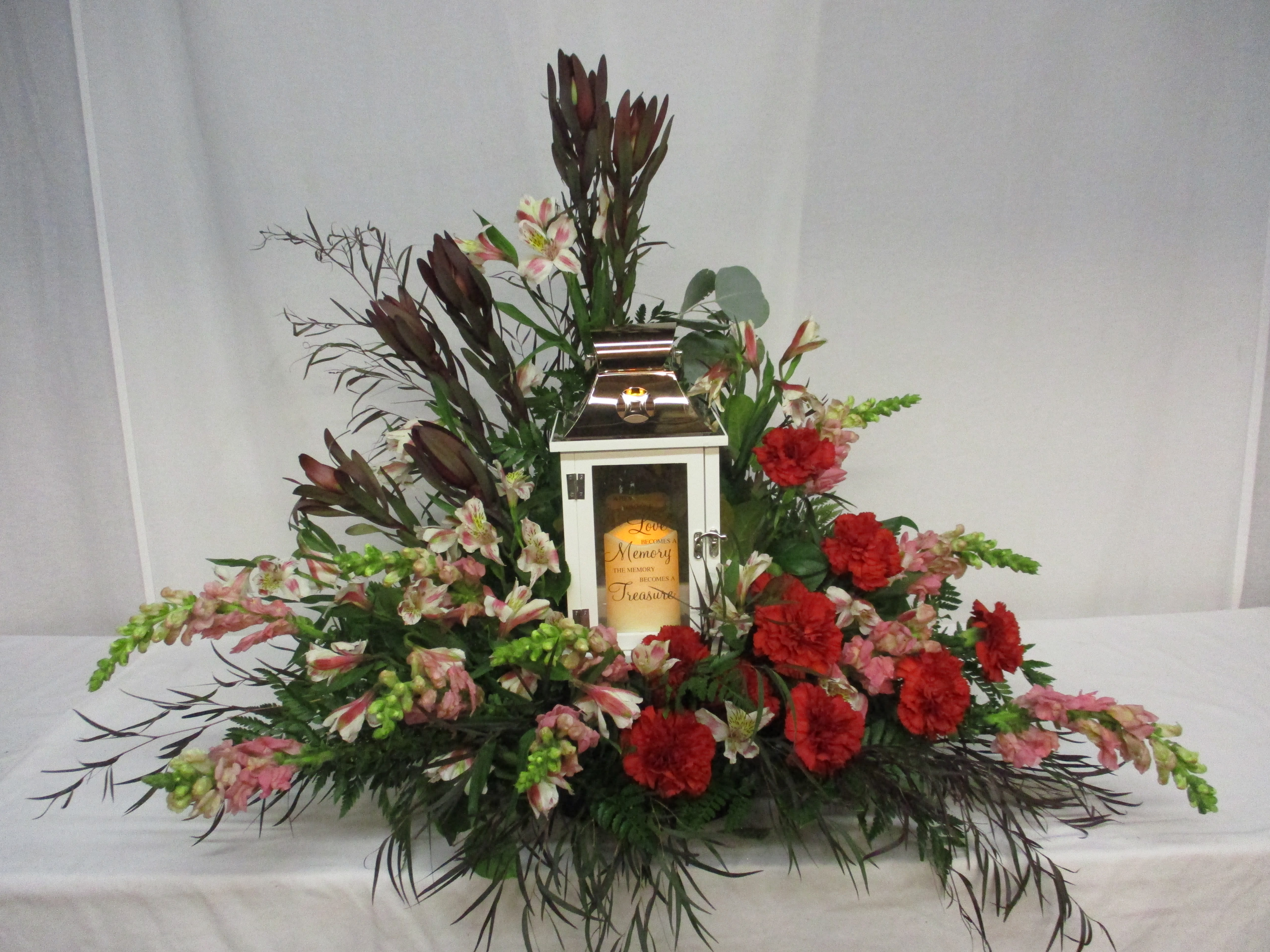 Floral arrangement around a white memorial lantern with red and pink flowers.
