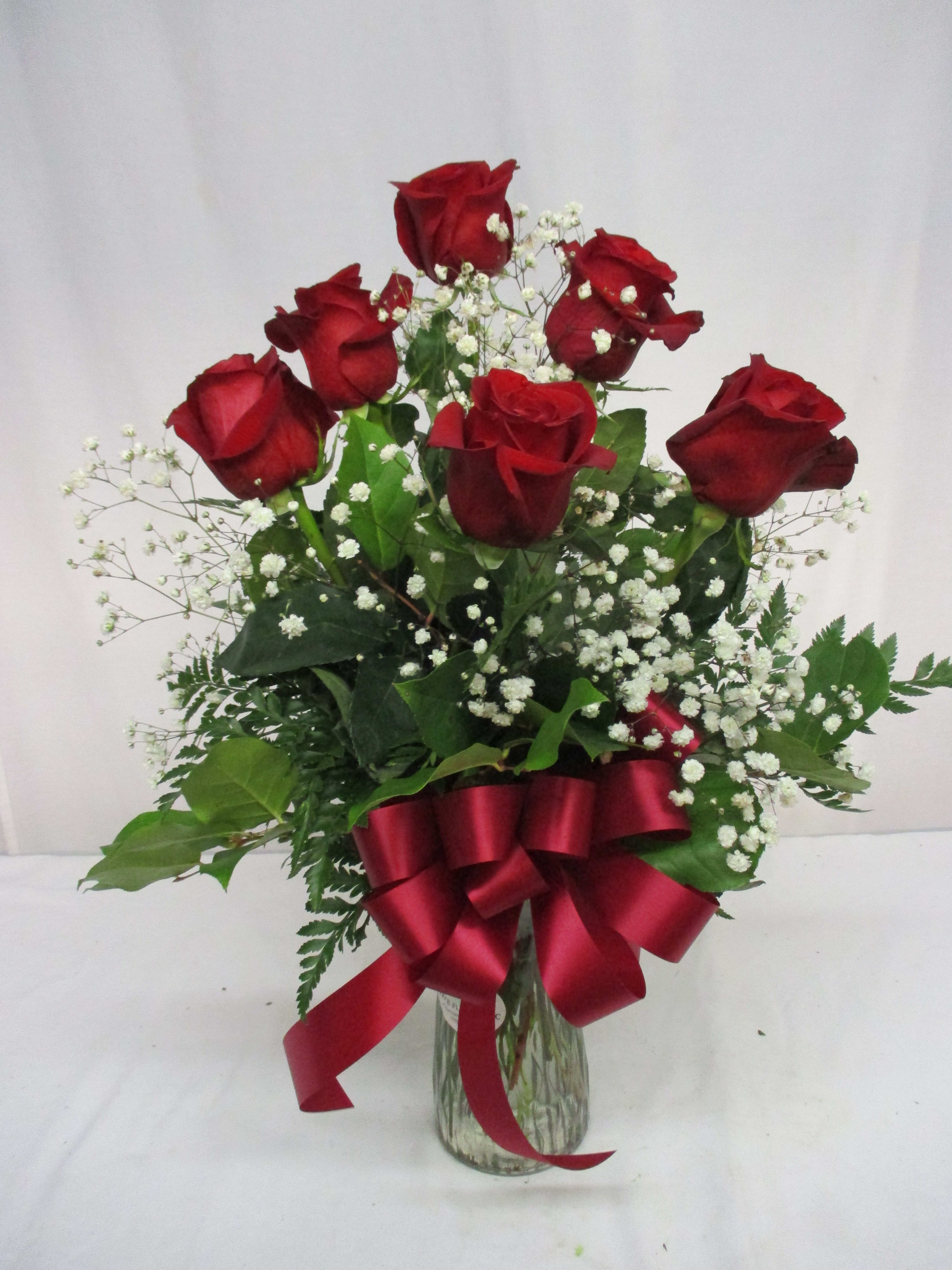 Red roses in a glass vase with baby's breath and a red ribbon