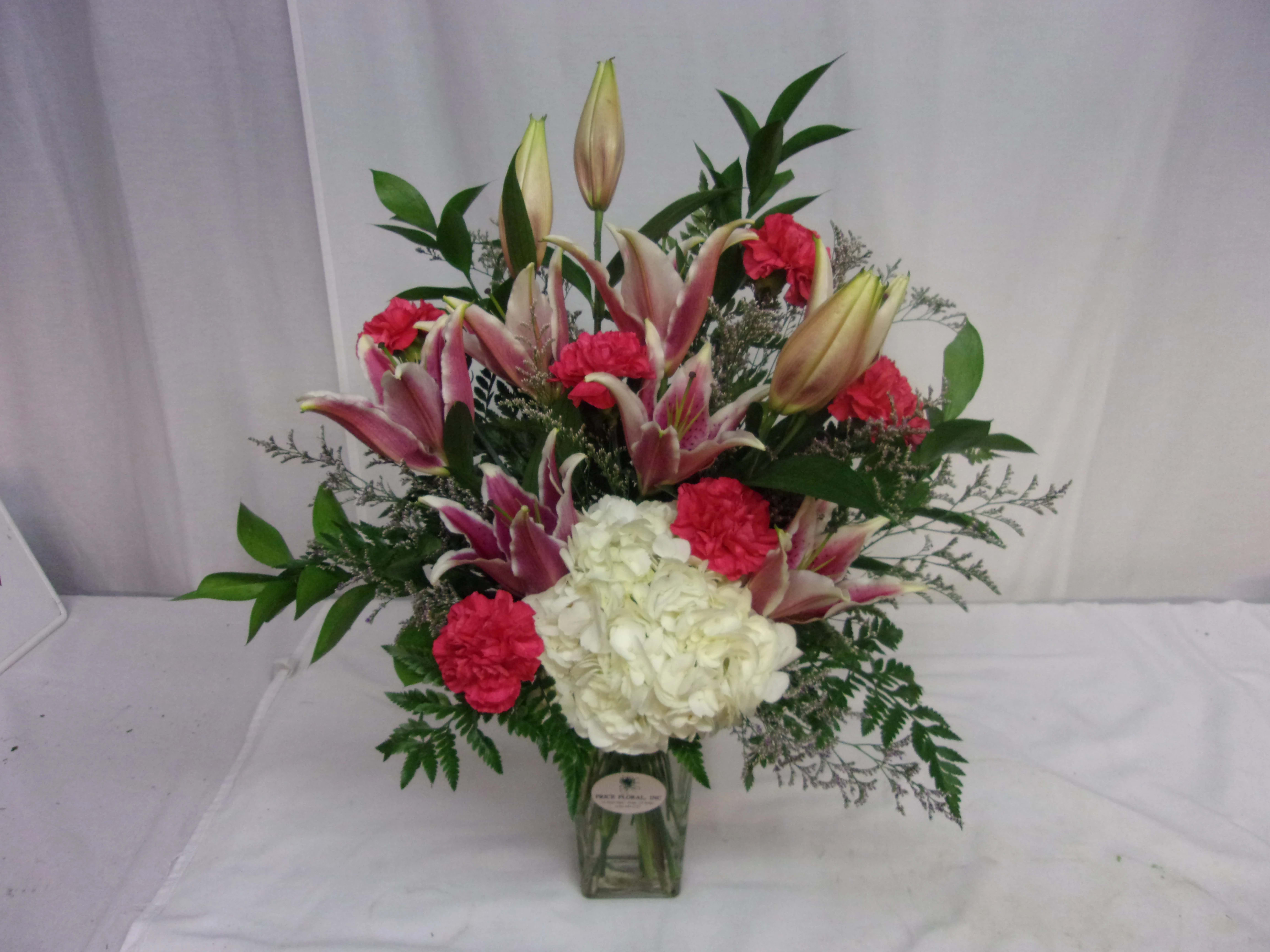 Pink lilies and red carnations in a glass vase with white hydrangea