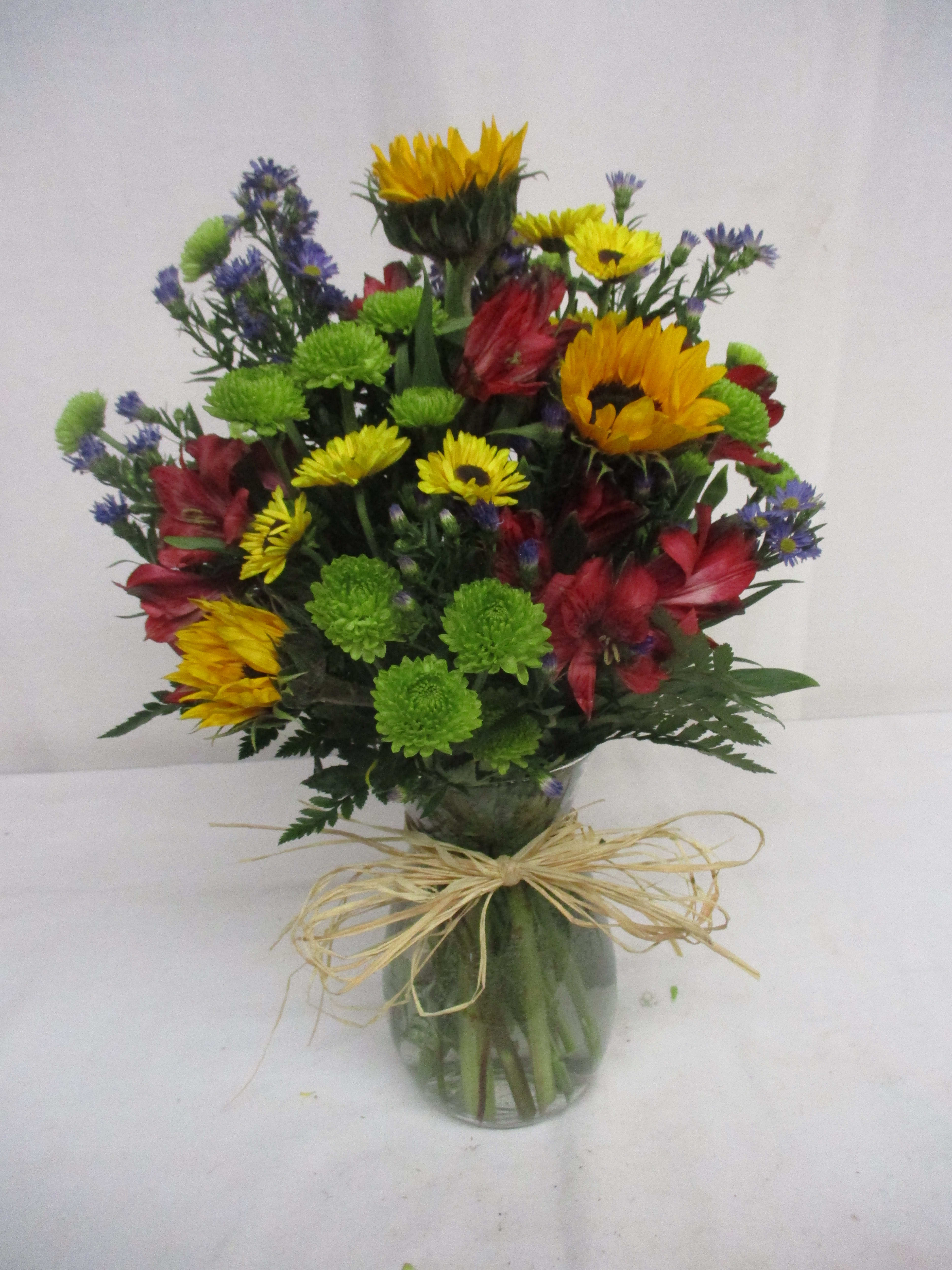 Mixed bouquet in a glass vase with bright yellow, red, green, and purple flowers