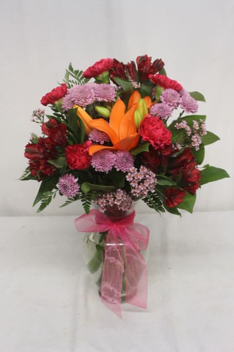 Bouquet of orange lilies and pink-red flowers in a glass vase with a pink ribbon