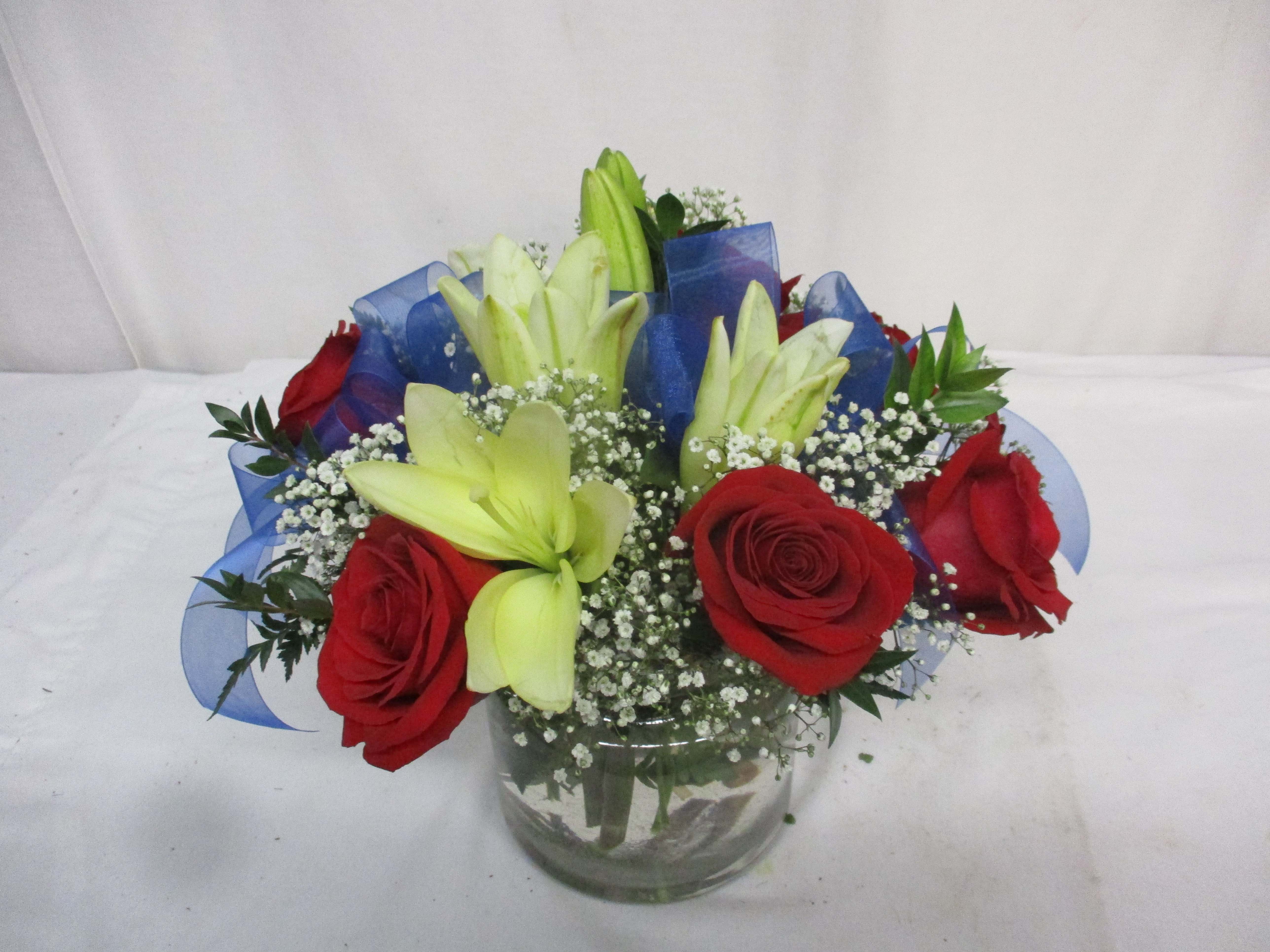 Red roses and pale lilies in a glass vase with blue ribbon