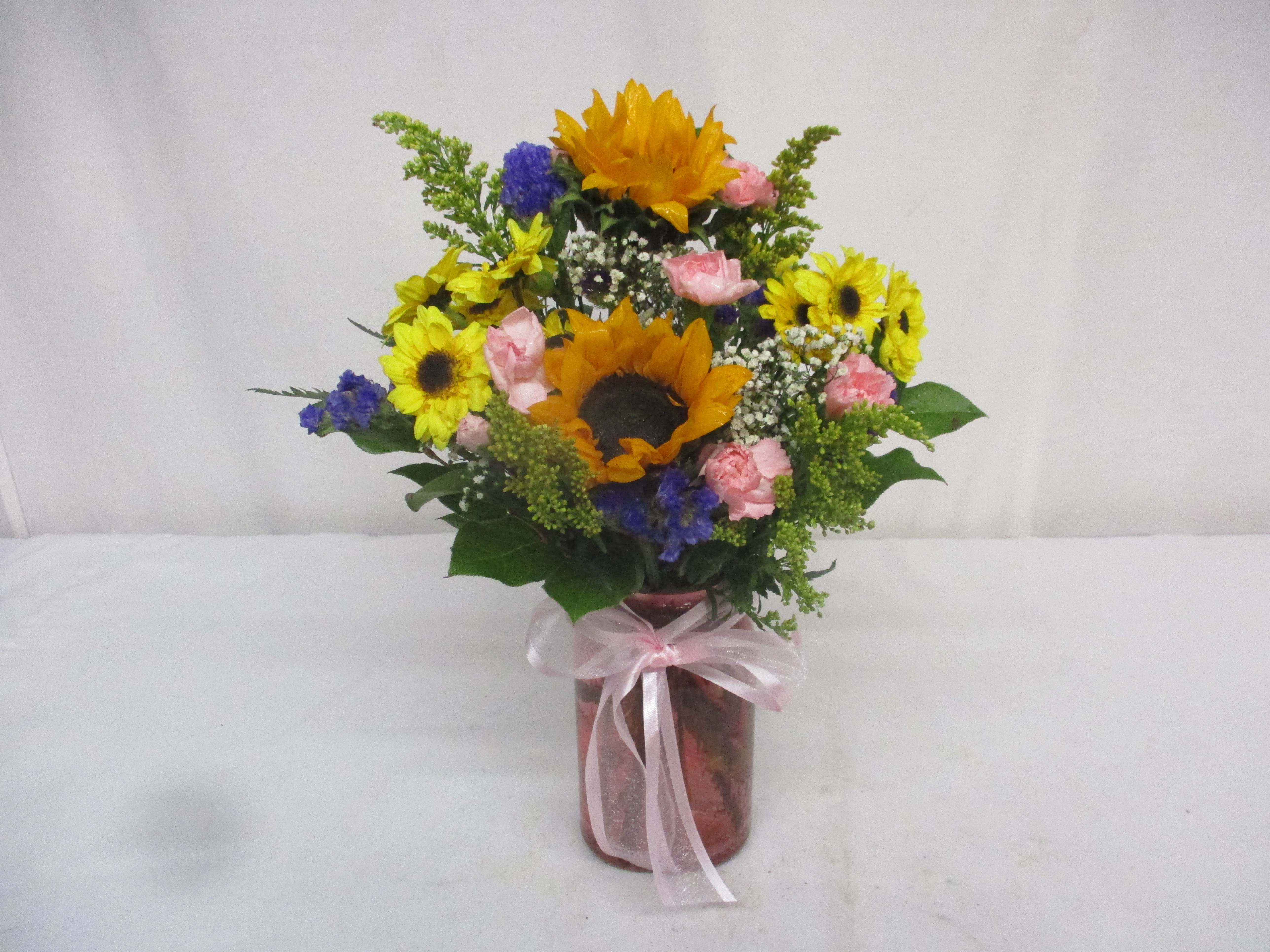 Bouquet of sunflowers, pink roses, and blue flowers in a glass vase