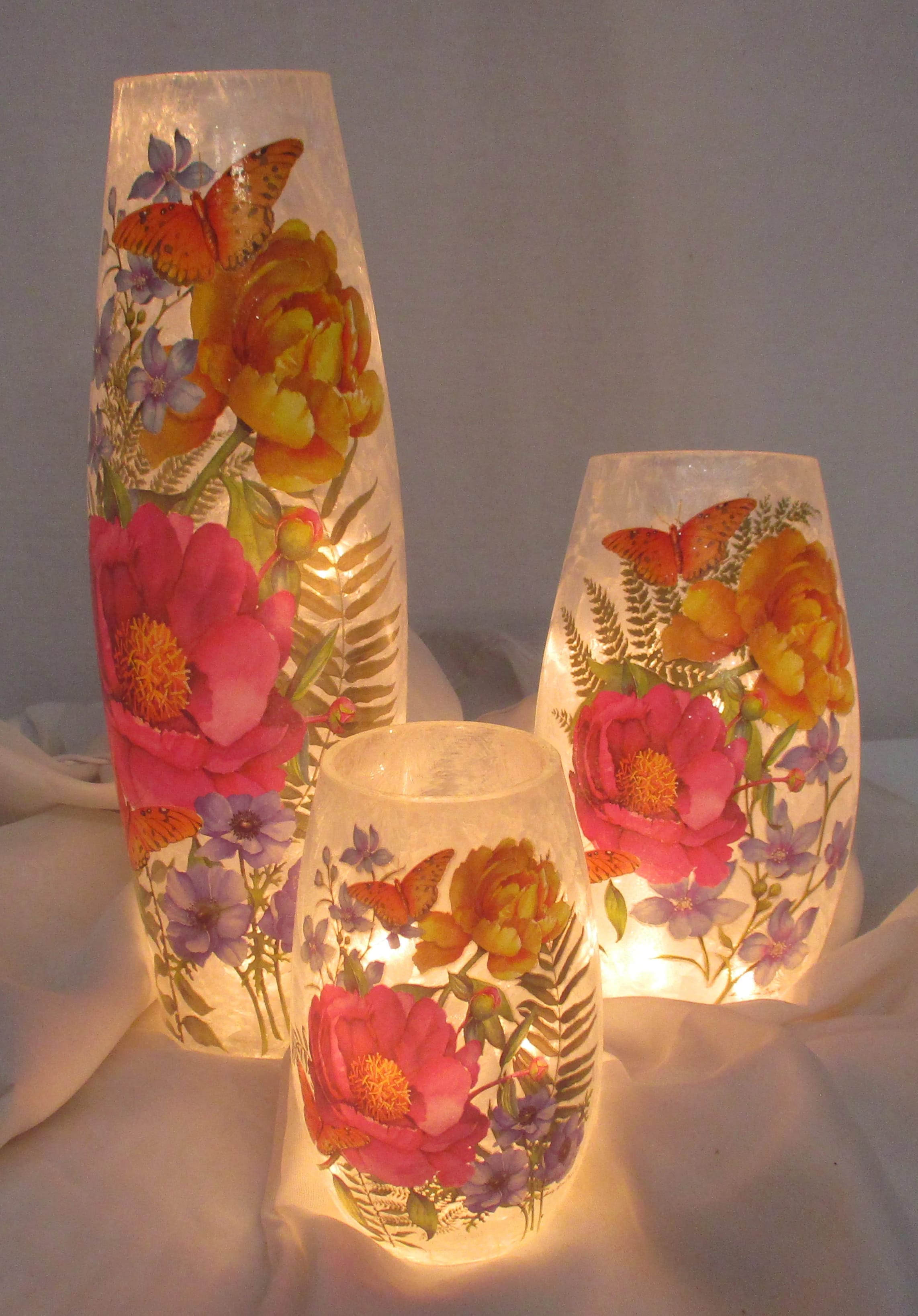 Three lit floral-patterned glass candle holders with butterflies