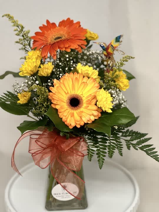 Orange and yellow gerbera daisies in a glass vase with a ribbon