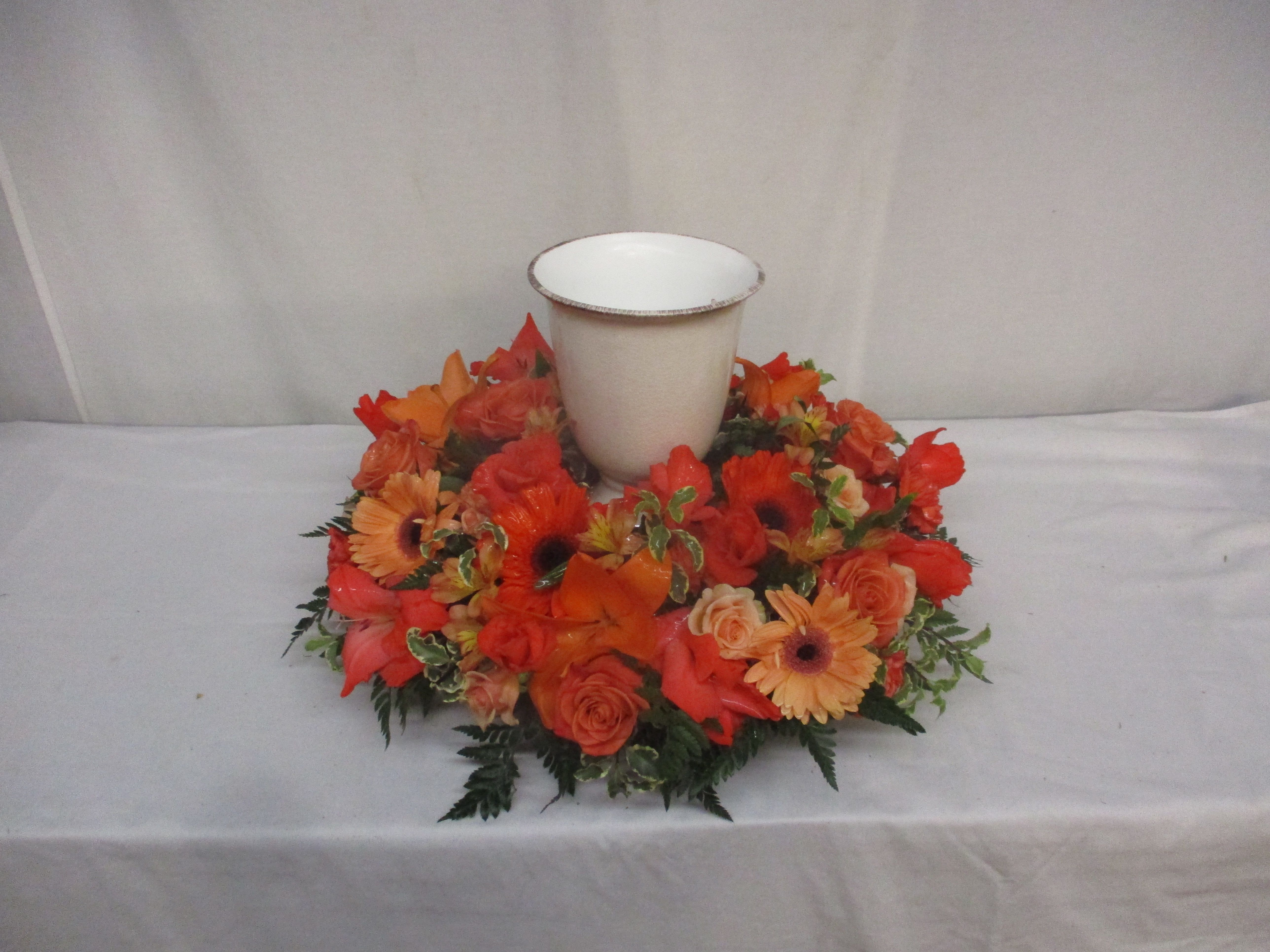 Orange floral wreath around a white urn-shaped vase