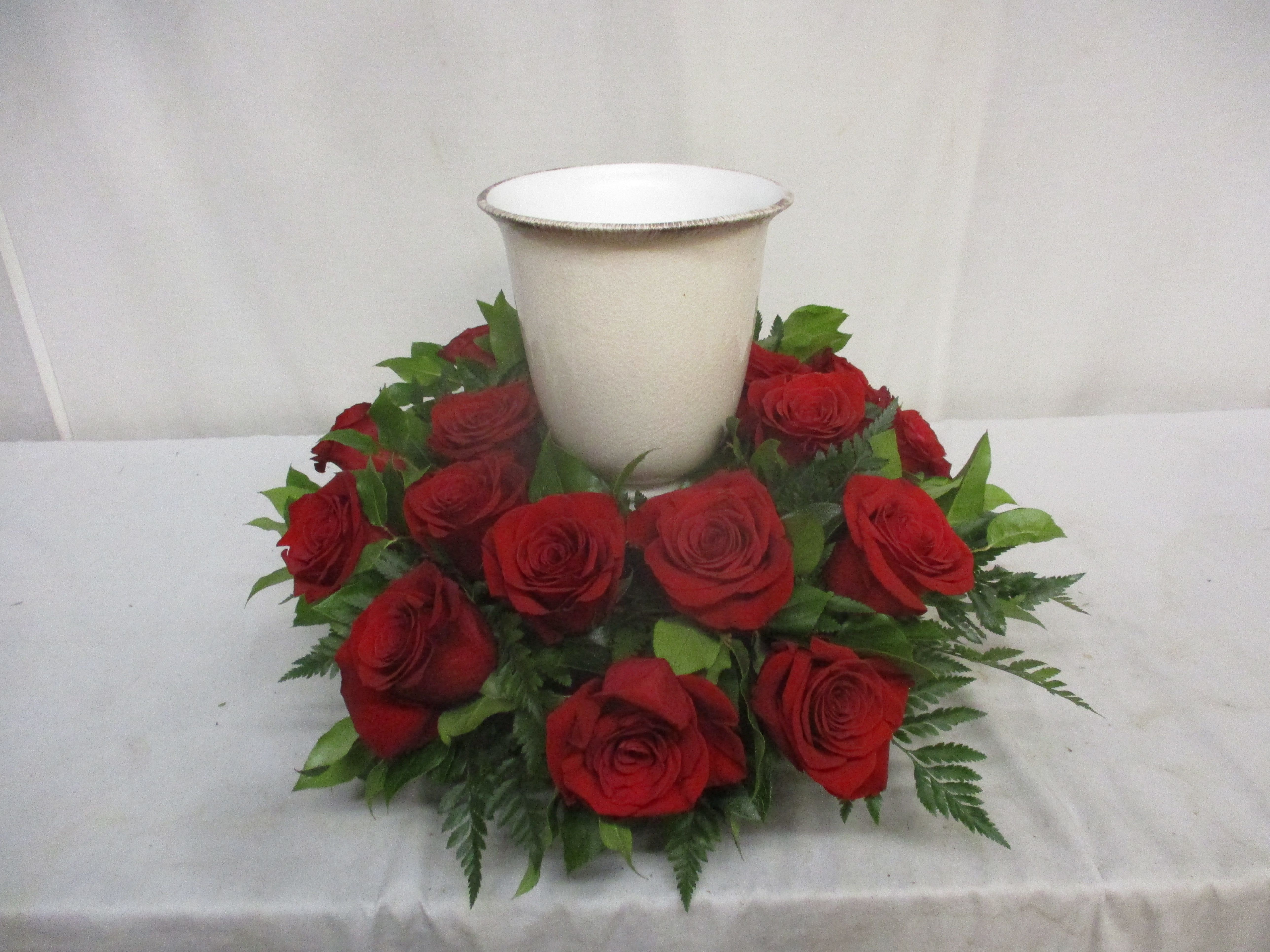 Red roses arranged around a white urn vase