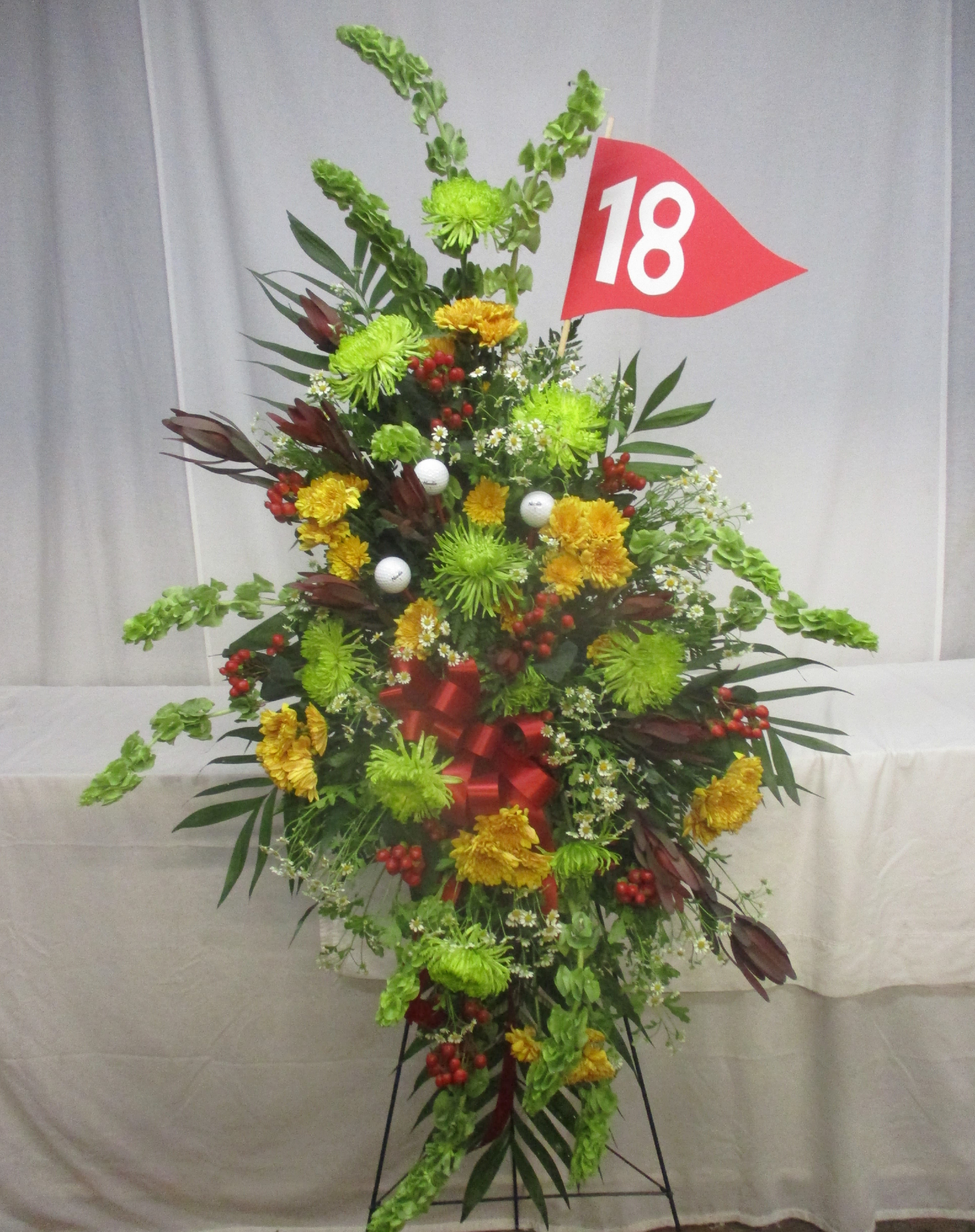 Tall floral standing spray with green and yellow flowers and a red number 18 flag