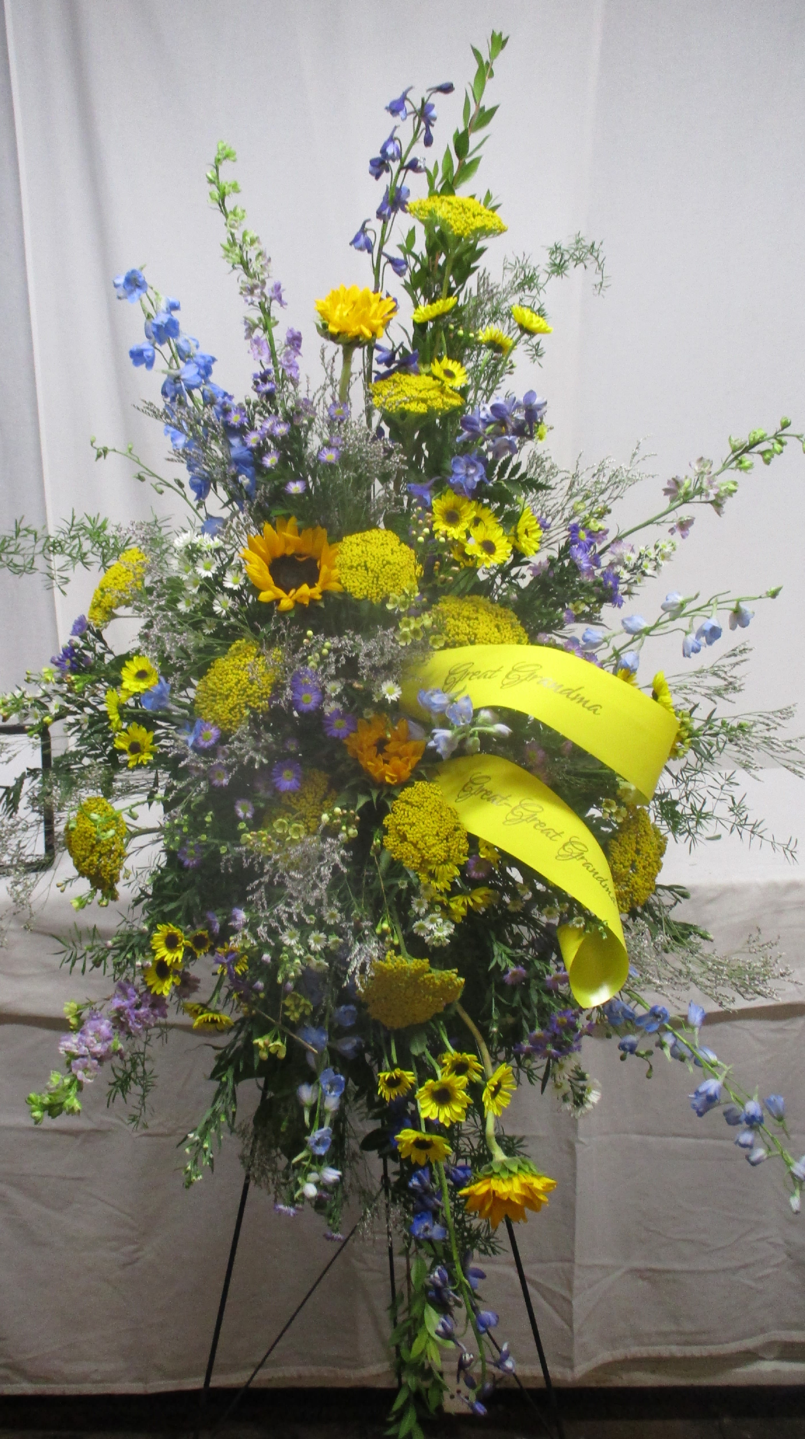 Tall standing floral spray with yellow and blue flowers on a black easel