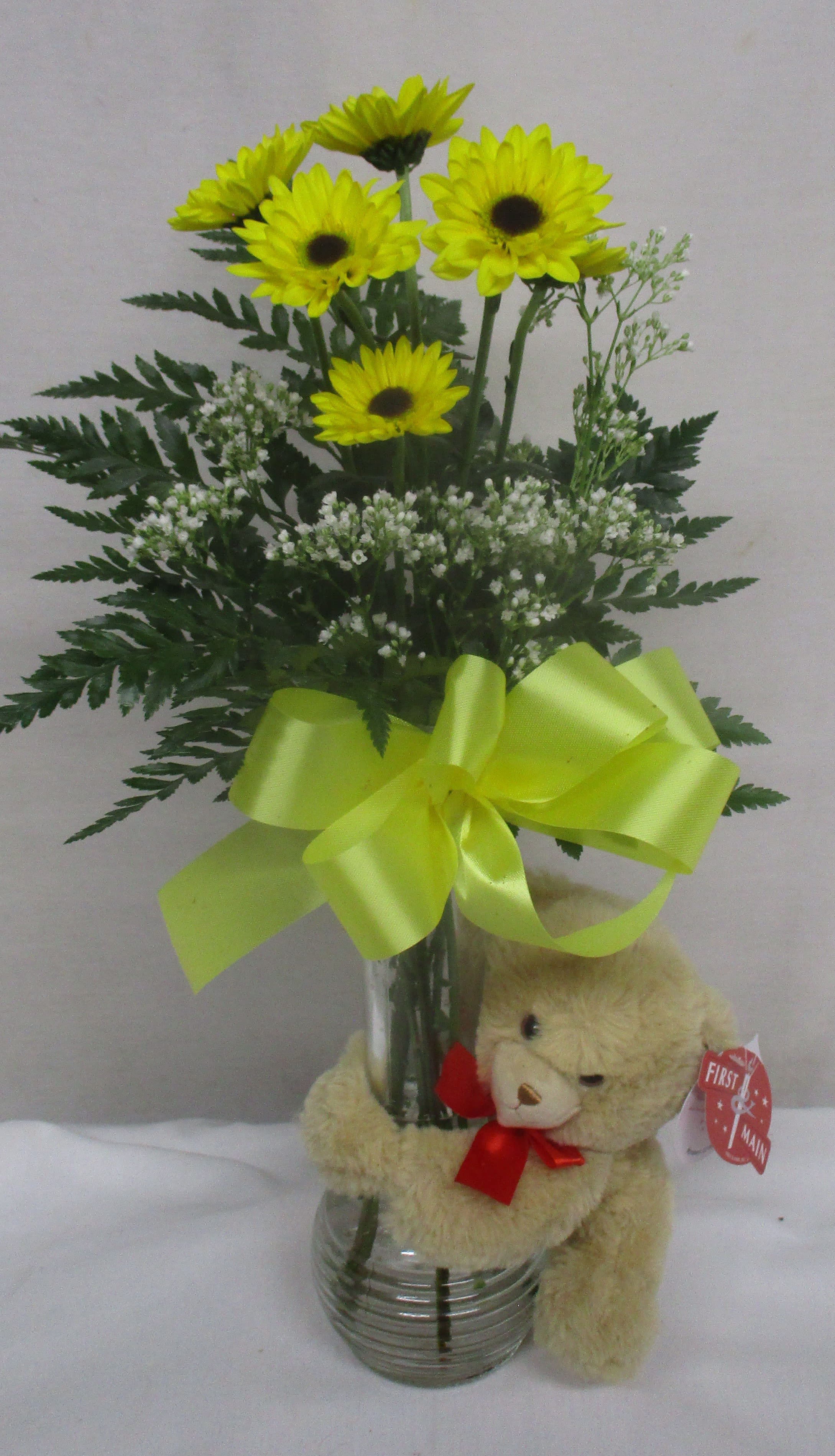 Yellow daisy bouquet in a glass vase with a teddy bear