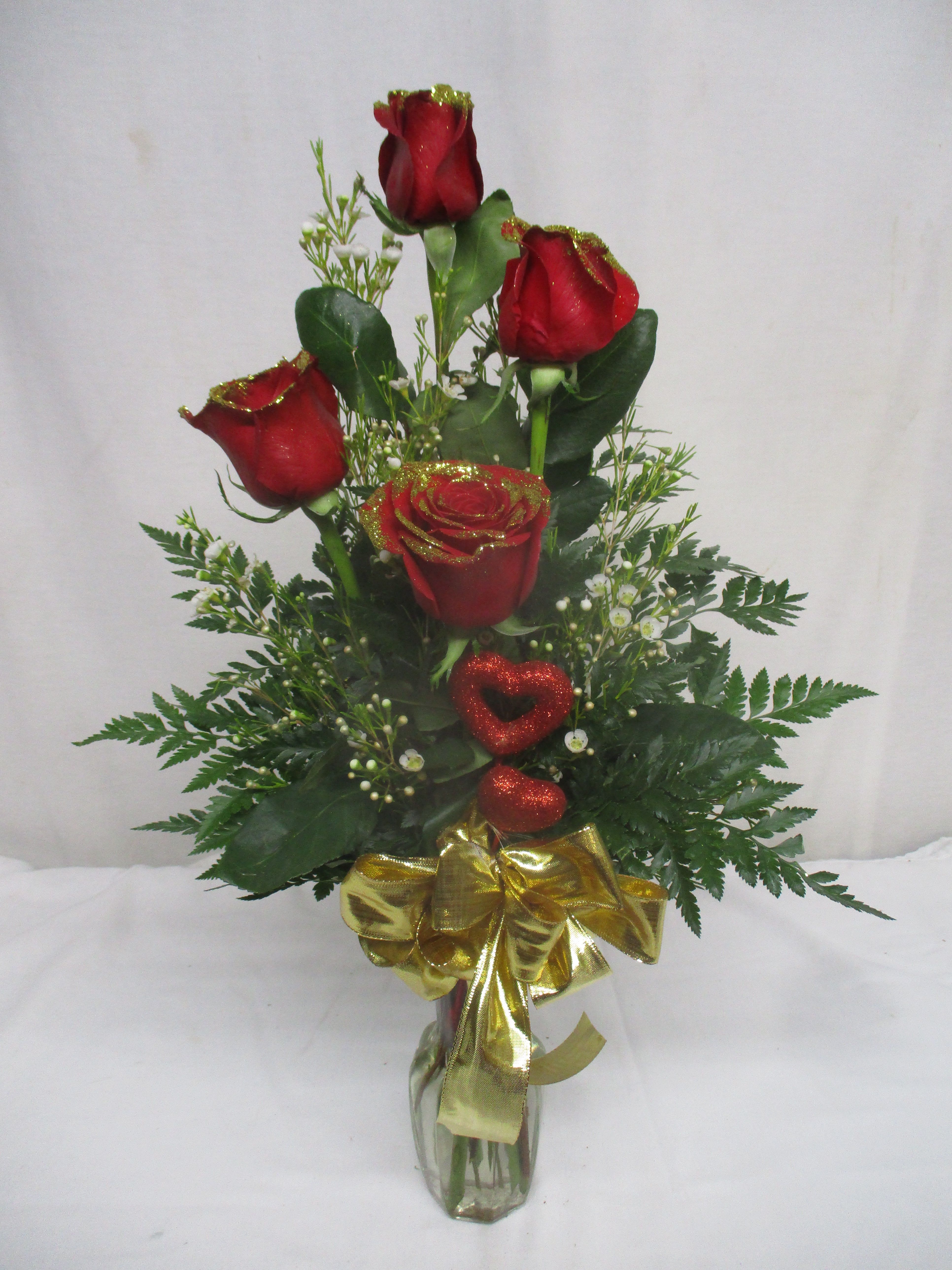 Red roses in a glass vase with a gold bow and glittery heart accents