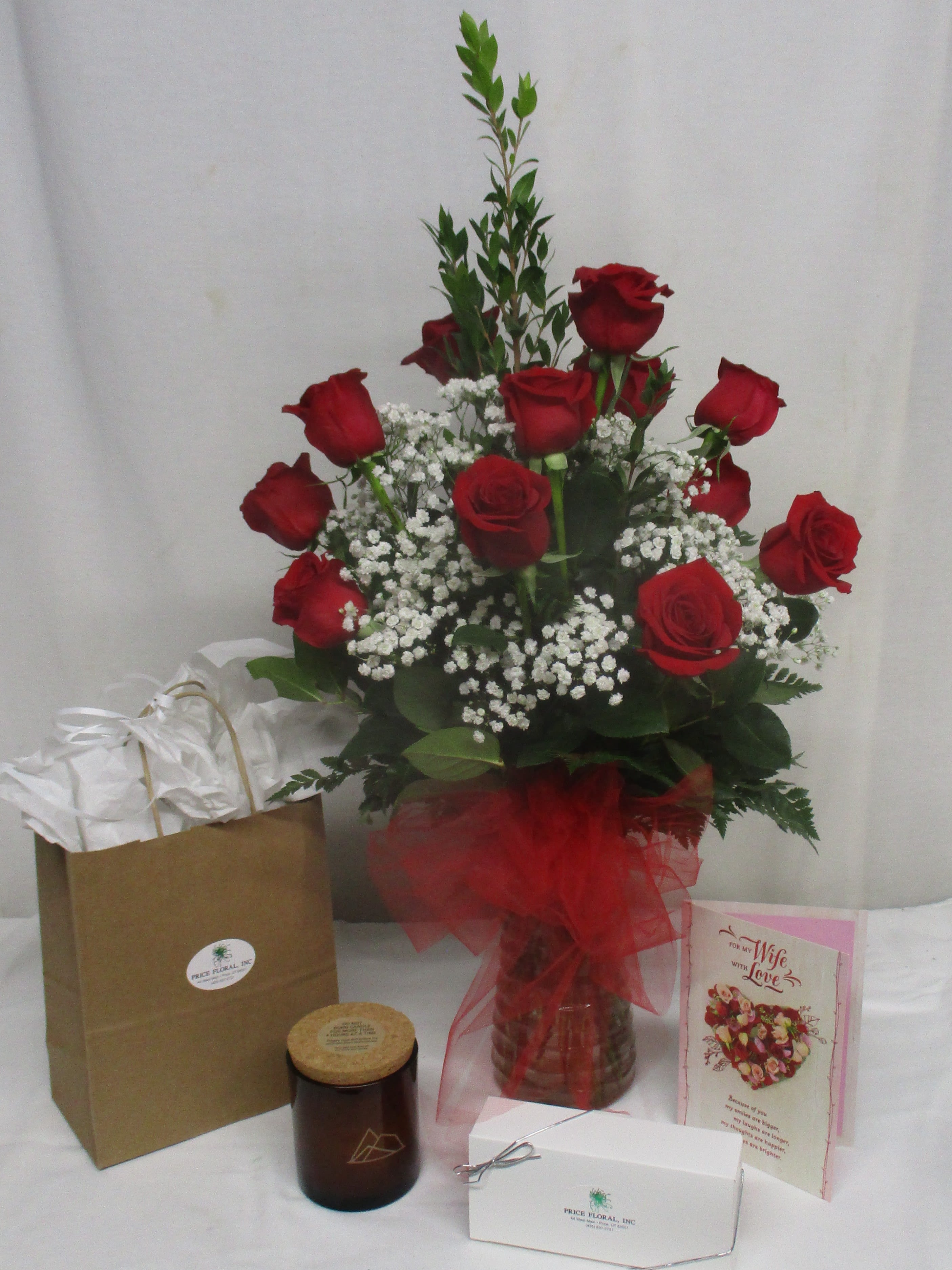 Red roses arranged in a glass vase with baby's breath and gift items nearby