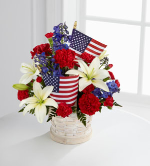 Red, white, and blue floral arrangement in a basket with small American flags