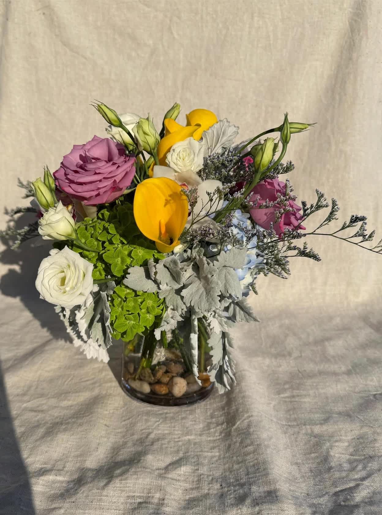 Mixed bouquet in a glass vase with yellow calla lilies, roses, and white blooms