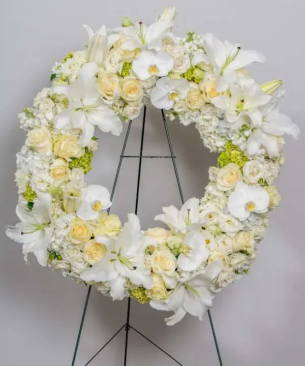 Graceful In White wreath - Their pure heart and peaceful spirit will live on in a gesture symbolizing the circle of eternal life. Our standing wreath of soothing white blooms and fresh greenery, expertly crafted by our local florists for a lush, full presentation, is a grand expression of your condolences, offering hope and serenity during a difficult time.. elegant wreath created from premium white blooms including hydrangea, lilies, orchids, and roses.