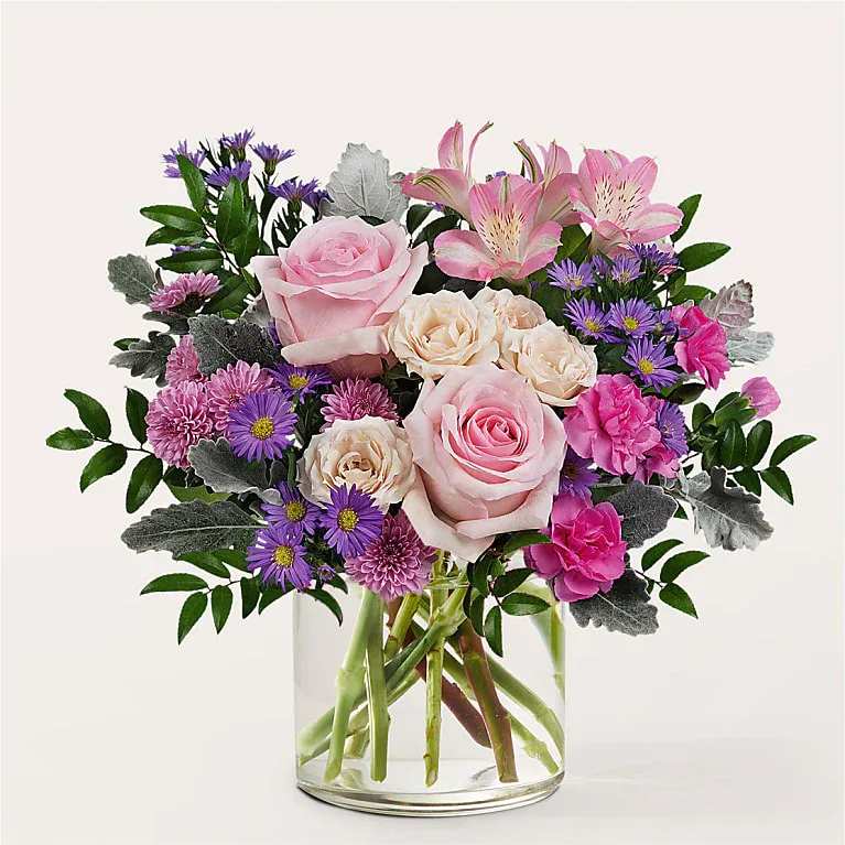 Pink and cream roses with purple flowers in a clear glass vase