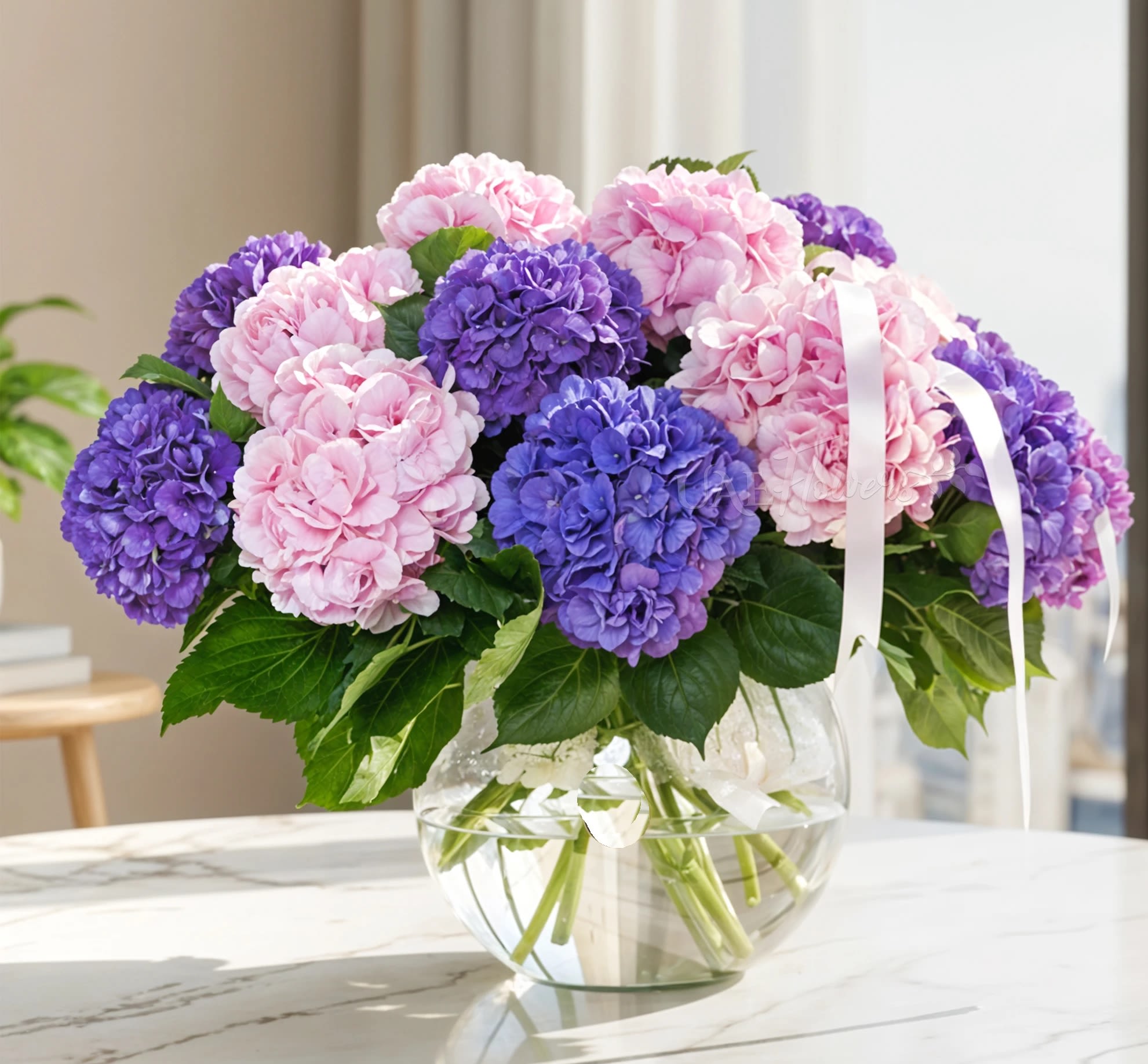 Pink and purple hydrangeas in a clear glass vase with a white ribbon