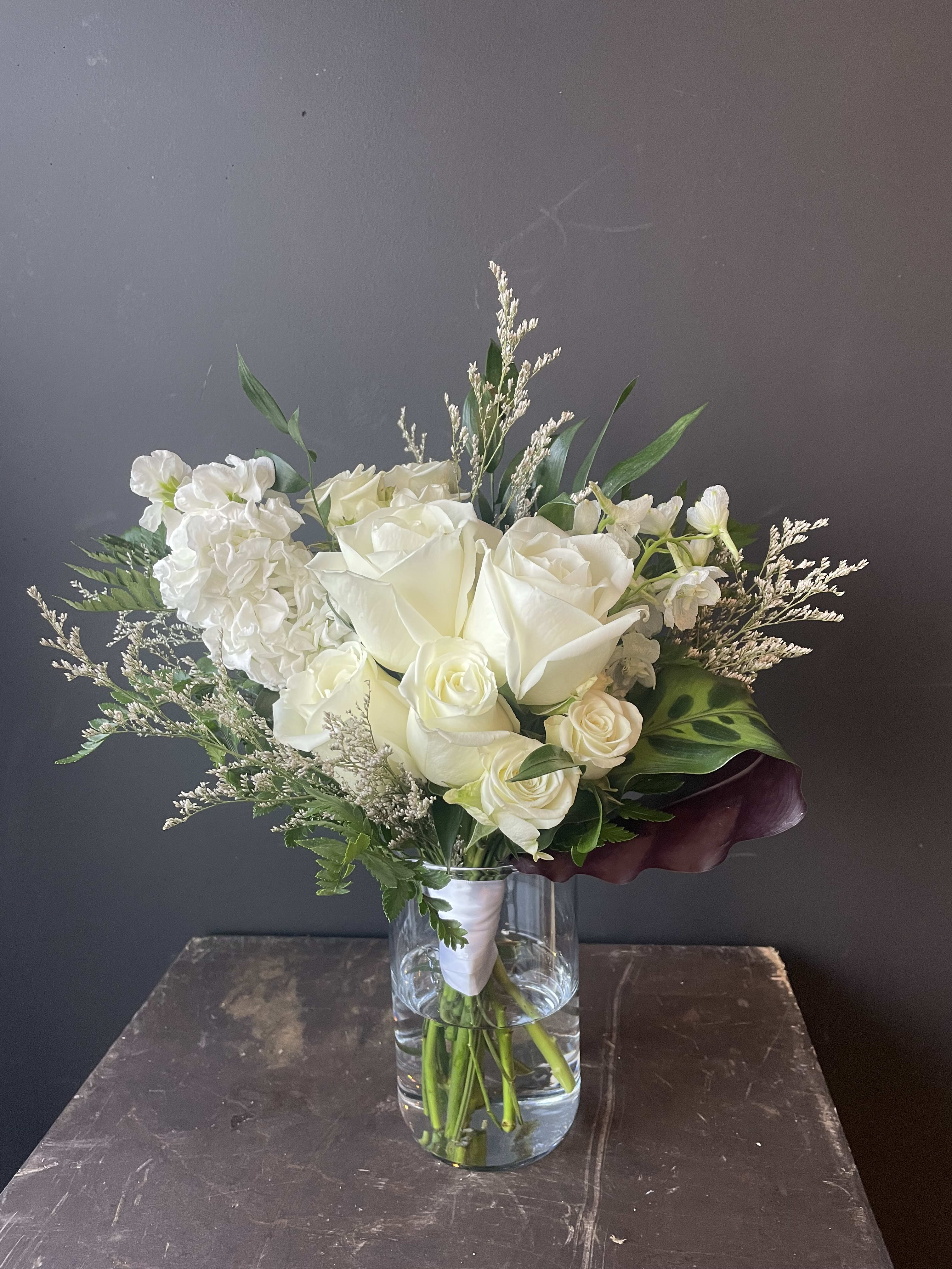White rose bouquet in a clear glass vase with mixed greenery