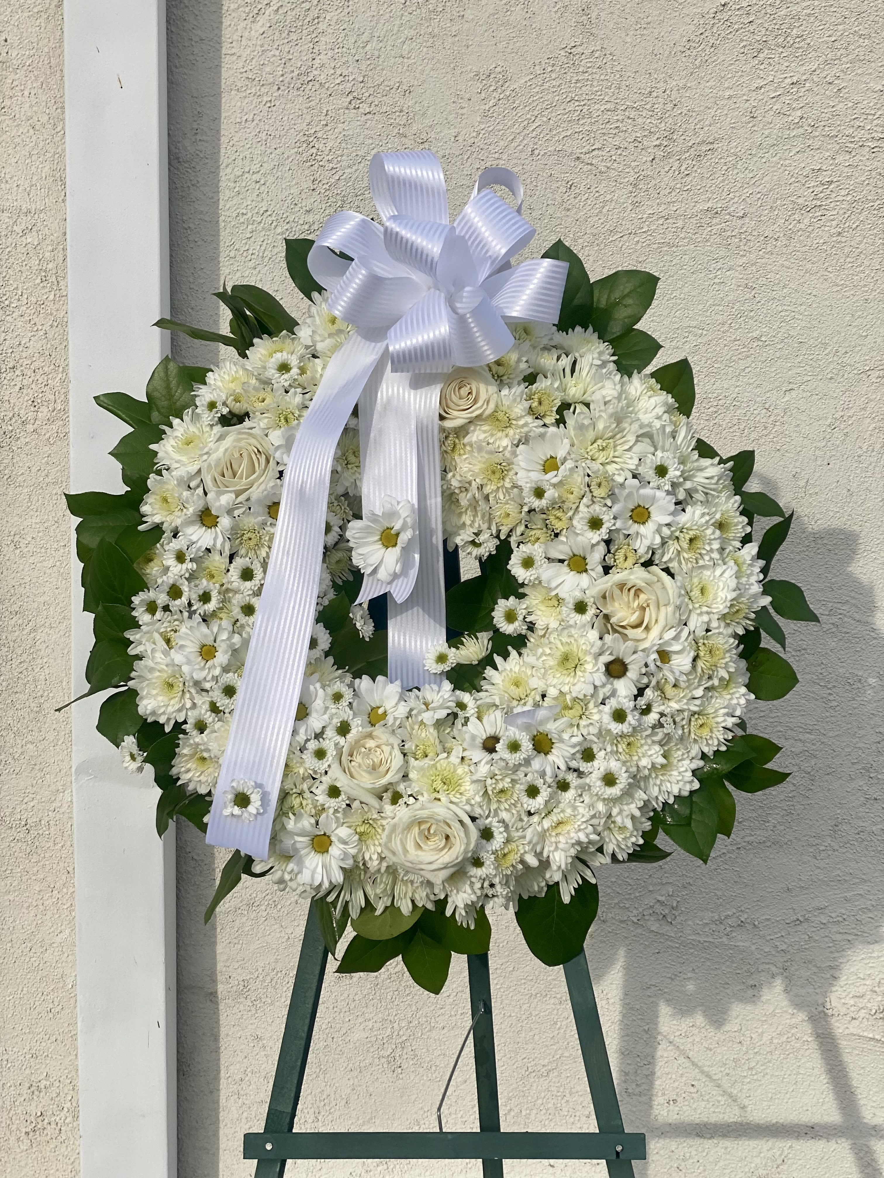White floral wreath with a ribbon bow on an easel