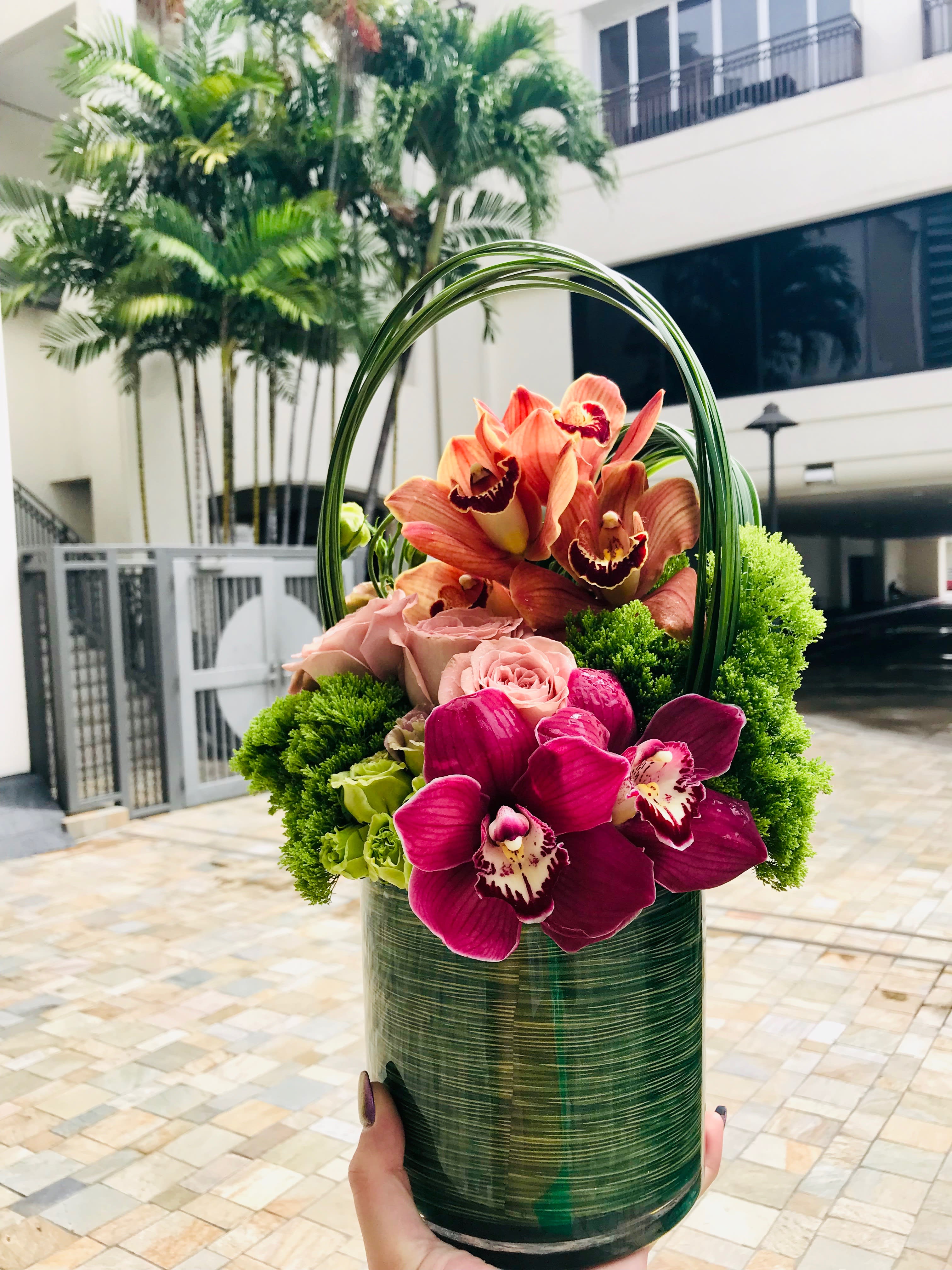 Orchid and rose arrangement in a green cylindrical container with a loop handle