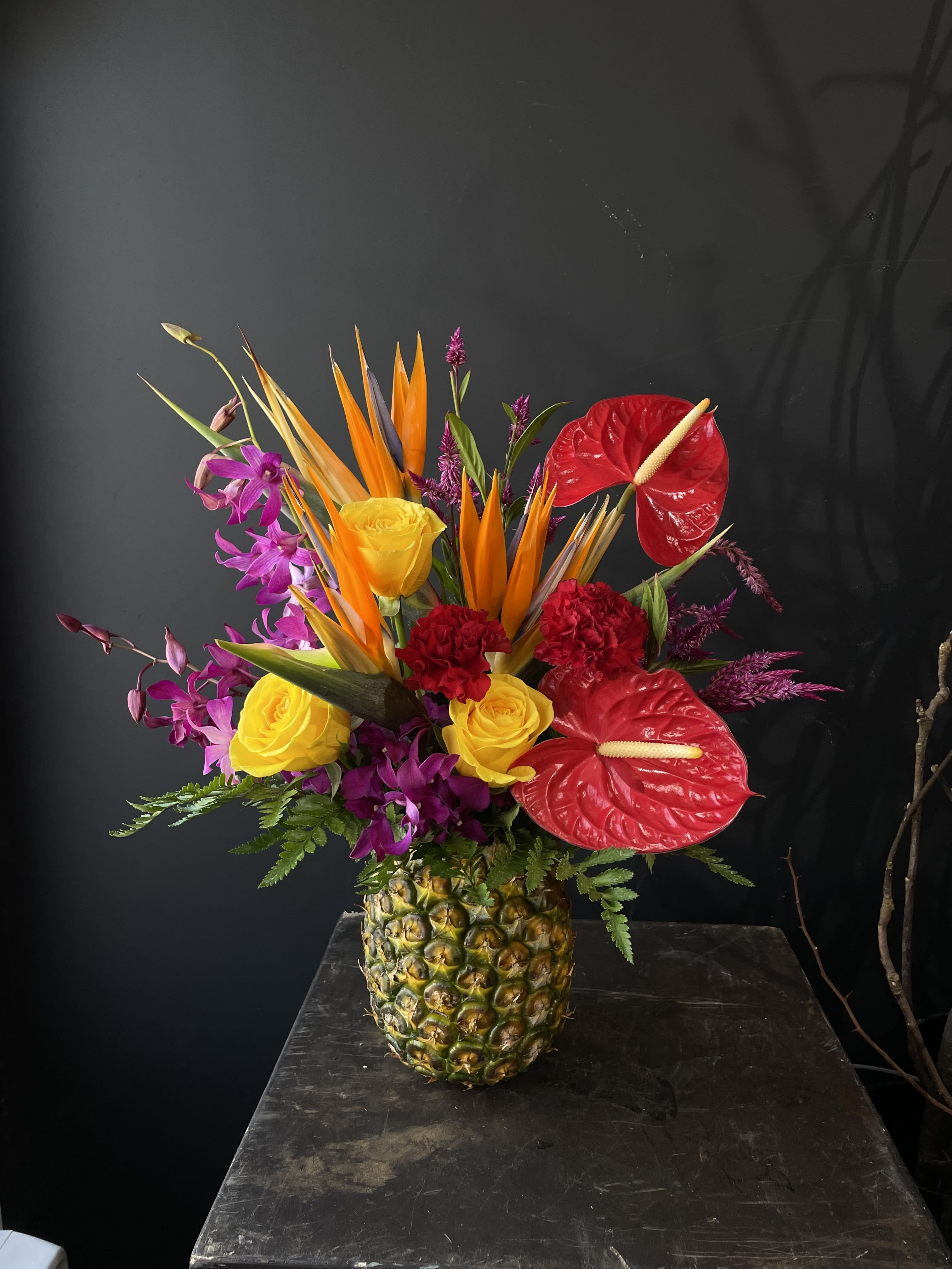 Tropical flower arrangement in a pineapple vase with red anthuriums and yellow roses