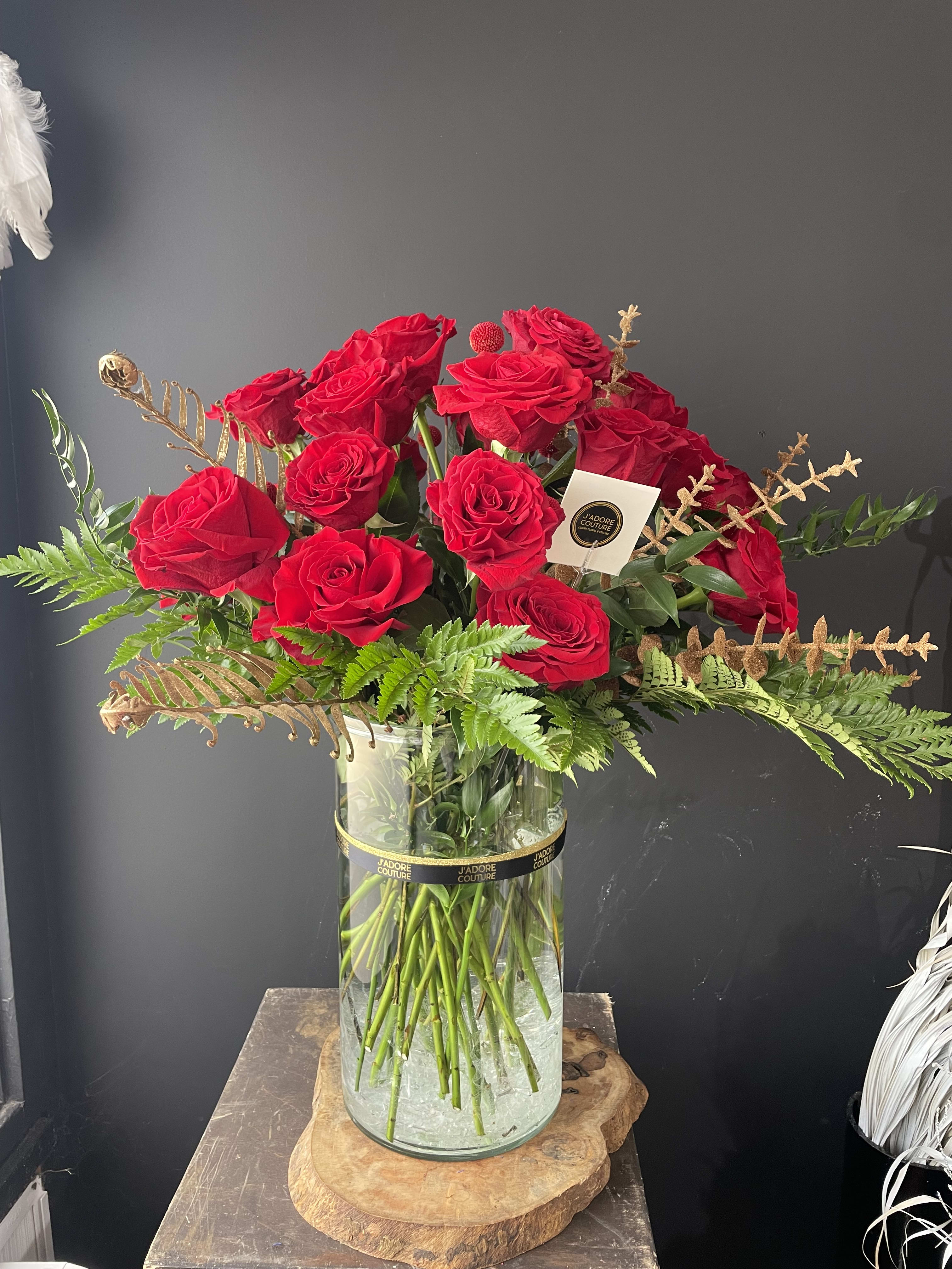 Red roses arranged in a clear glass vase with fern accents