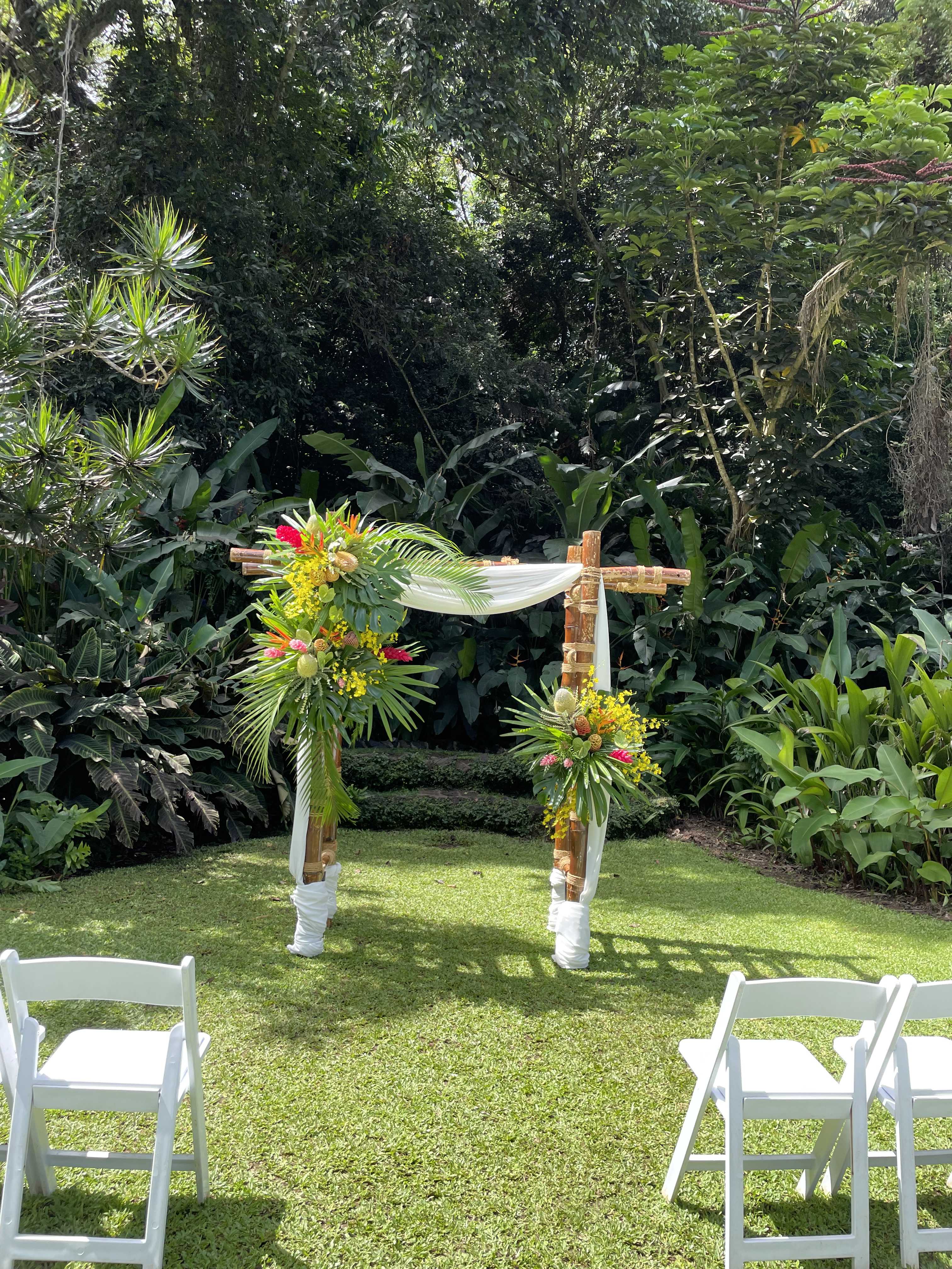 Tropical floral arch with white drape in a garden setting