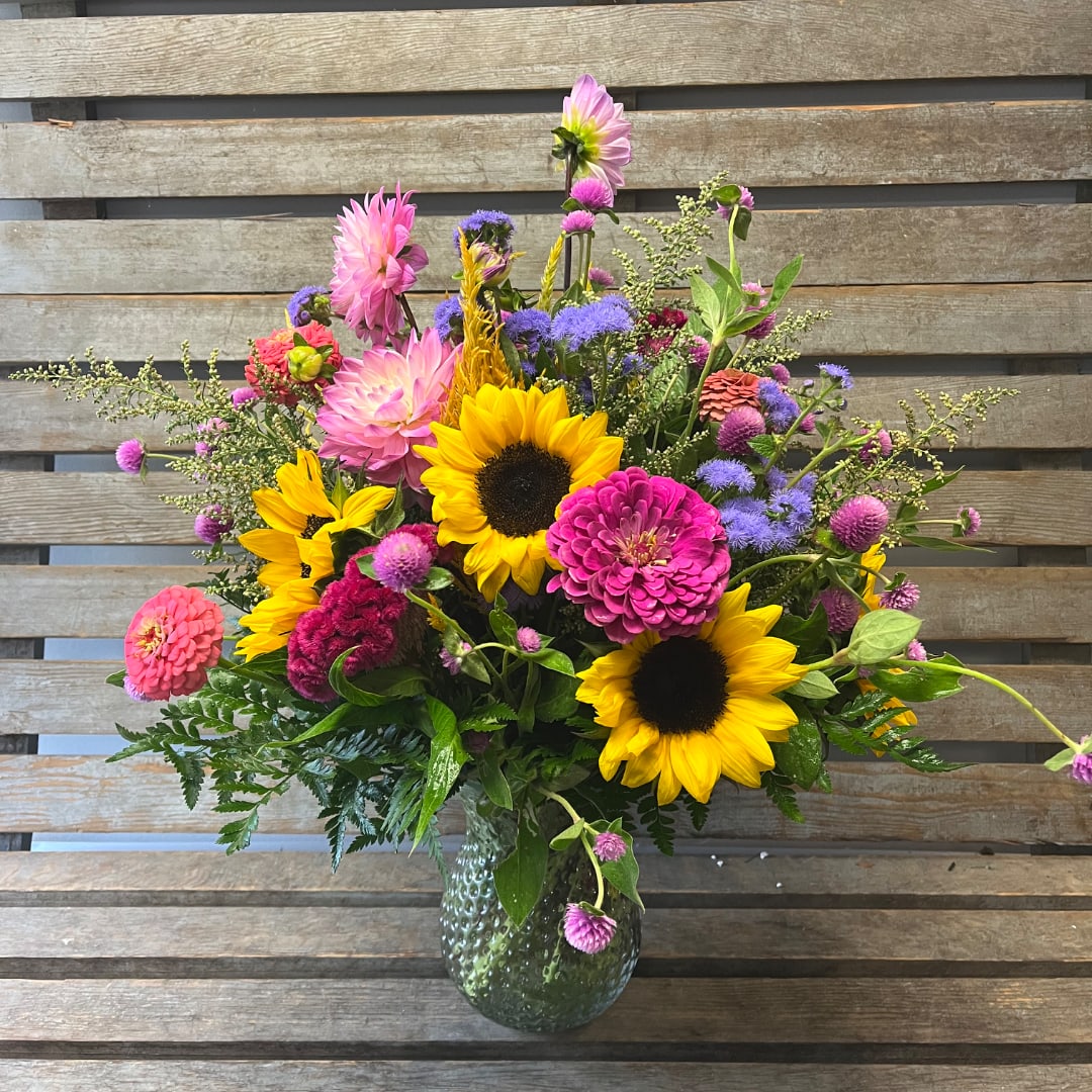 Colorful mixed bouquet with sunflowers, zinnias, and purple blooms in a glass vase