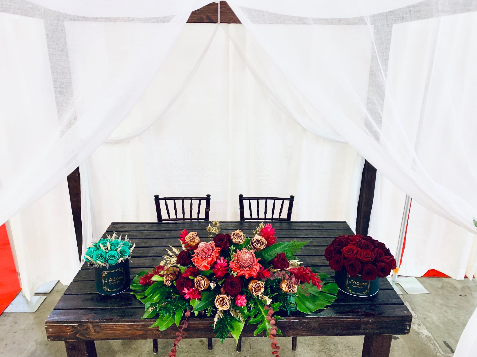 Three floral arrangements on a table, including red roses and turquoise roses in black containers