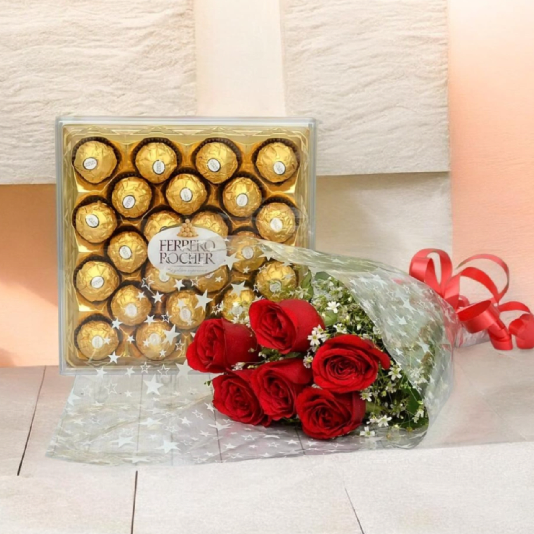 ROSAS ROJAS FERRERO ROCHER - A petite bouquet of red roses paired with a box of Ferrero Rocher makes a classic romantic gift for Valentine's Day, an anniversary, or to say "I love you" on a special birthday. The red roses and bright red ribbon create an immediate feeling of passion and warmth, while the gold-wrapped chocolates add a celebratory, indulgent touch - the kind of present that makes the person you're thinking of feel seen and adored.  The arrangement features a small handful of red roses accented with tiny white filler flowers and fresh greenery, wrapped in clear cellophane printed with a subtle star pattern and finished with a bright red bow. The Ferrero Rocher chocolate box sits behind the bouquet, its metallic gold packaging contrasting beautifully with the deep crimson blooms for a balanced, polished presentation. This compact gift set is easy to hand-deliver or display, perfect when you want a meaningful, elegant gesture without being over the top.  Ideal for a romantic partner, close friend, or anyone who deserves a sweet, intimate surprise, this duo pairs floral beauty with a classic chocolate treat. Care is simple: keep the roses in fresh water and out of direct heat to extend their vase life; chocolates are best enjoyed at room temperature soon after delivery.
