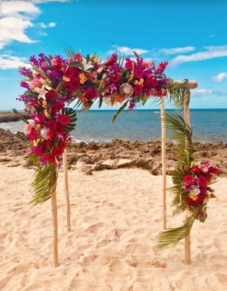 Floral arch with red, pink, and white flowers on a beach