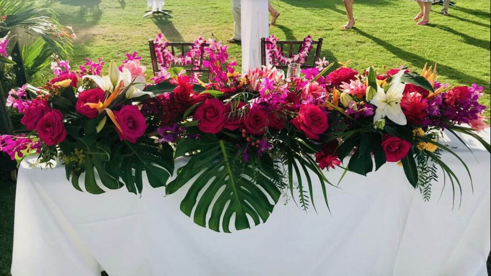 Long tropical floral centerpiece with pink roses and white lilies on a table