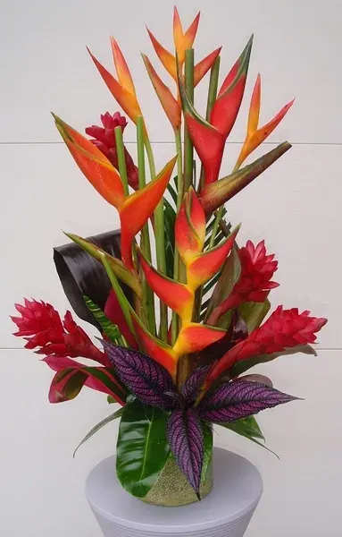 Tropical bouquet with orange and red heliconia in a gold vase