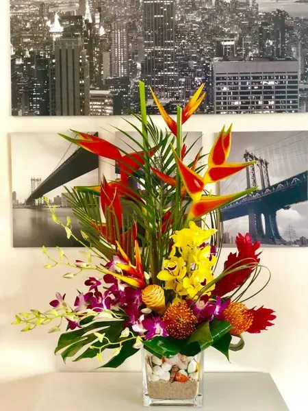 Tropical flower arrangement in a clear square vase with red, yellow, and purple blooms