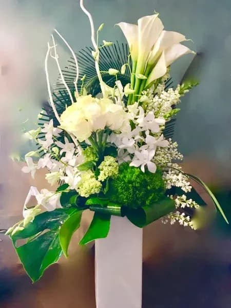 White floral arrangement with calla lilies and orchids in a tall vase