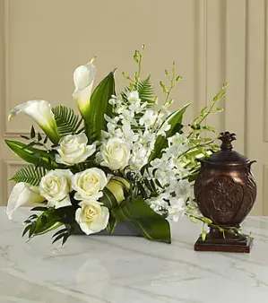 White roses and calla lilies arranged with white orchids in a dark vase