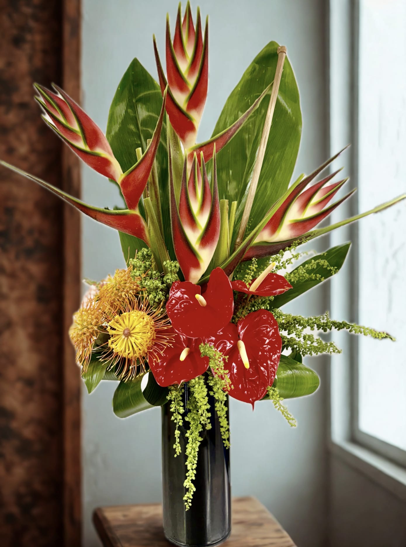 Tropical arrangement with red heliconia and red anthuriums in a tall black vase