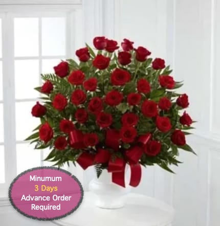 Red roses arranged in a white vase with a red ribbon