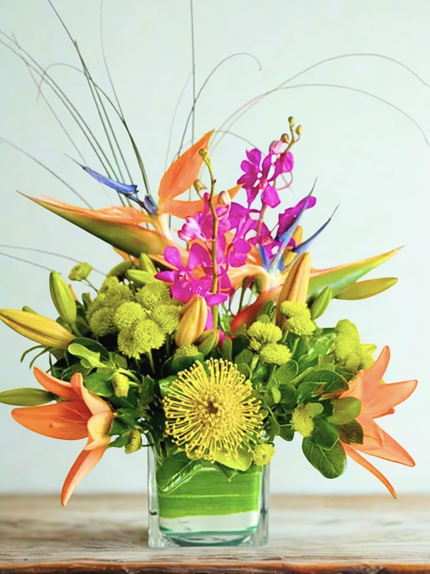 Tropical bouquet with orange bird-of-paradise and pink orchids in a glass vase