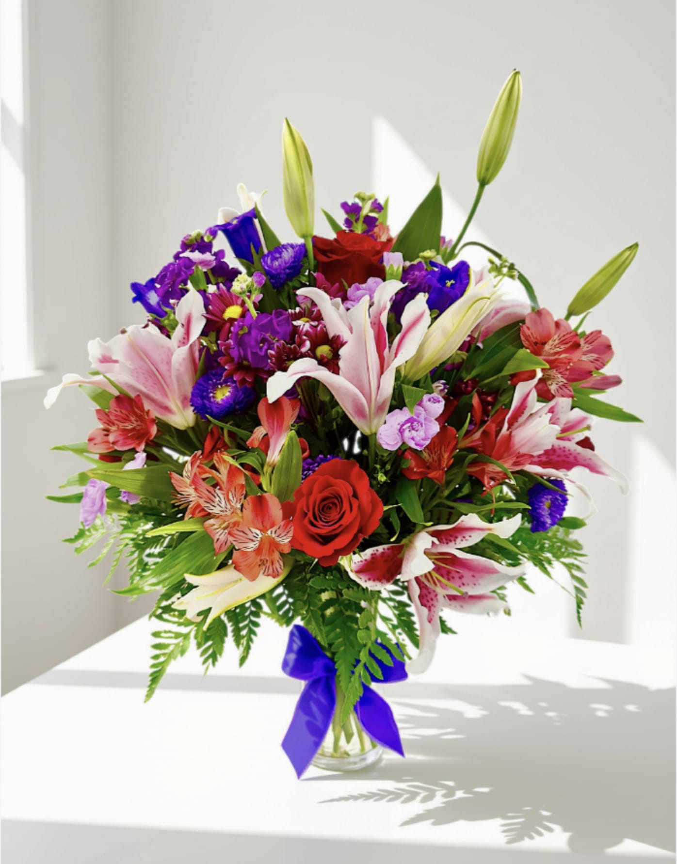 Mixed bouquet of lilies, roses, and purple flowers in a glass vase