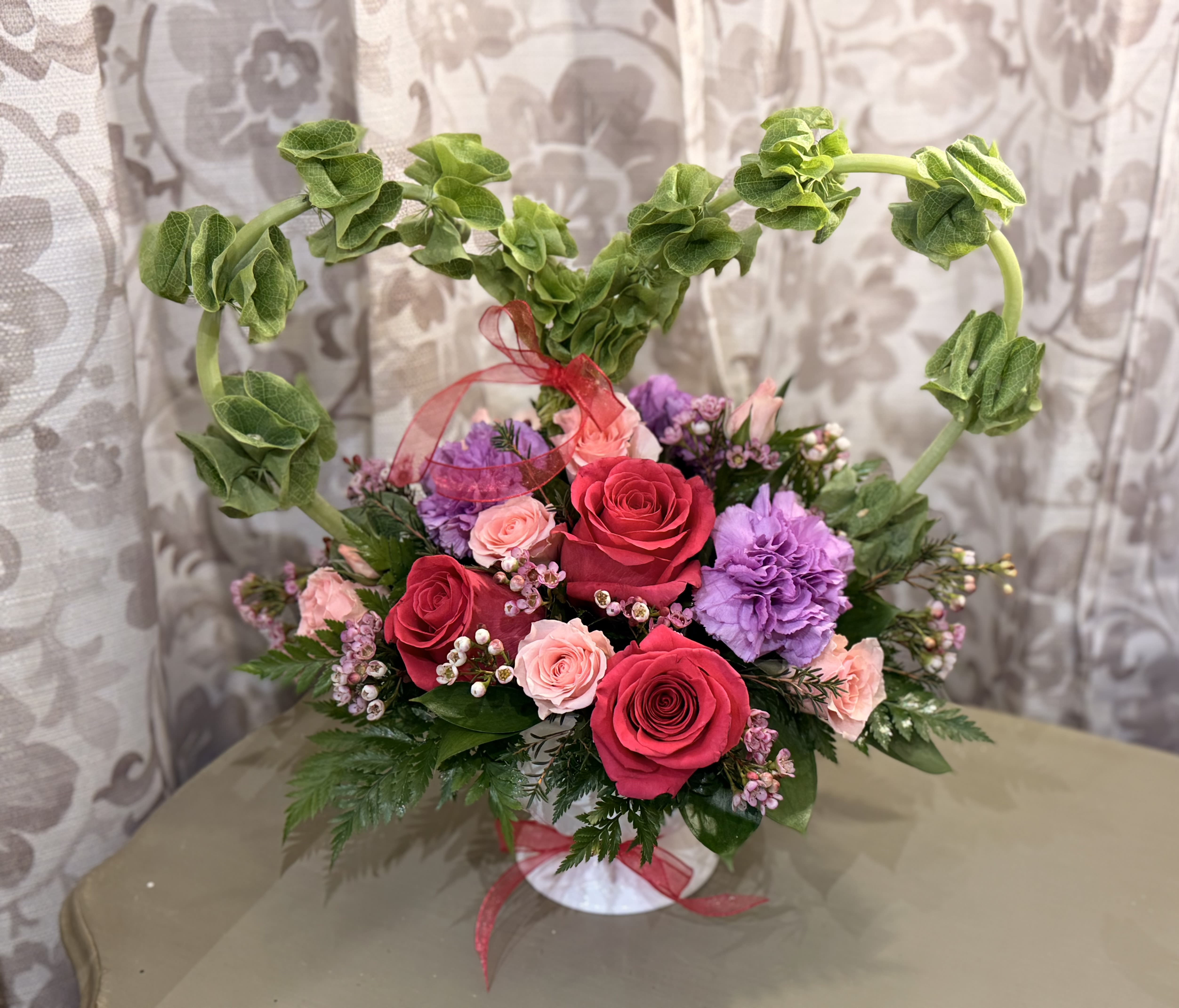 Heart-shaped floral arrangement with roses and purple carnations