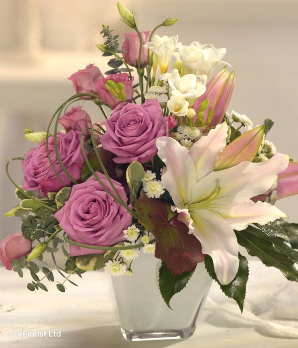 Lavender Grace - An elegant blend of soft lavender roses, fragrant pink lilies, white freesia, and delicate accent blooms arranged in a modern glass vase. Lavender Grace offers a beautiful combination of color, fragrance, and sophistication, making it a lovely choice for birthdays, anniversaries, sympathy, or just because.  Please note: Flower varieties and colors may vary based on seasonal availability. Substitutions may be made with flowers of equal or greater value while maintaining the overall style, color palette, and feel of the arrangement.