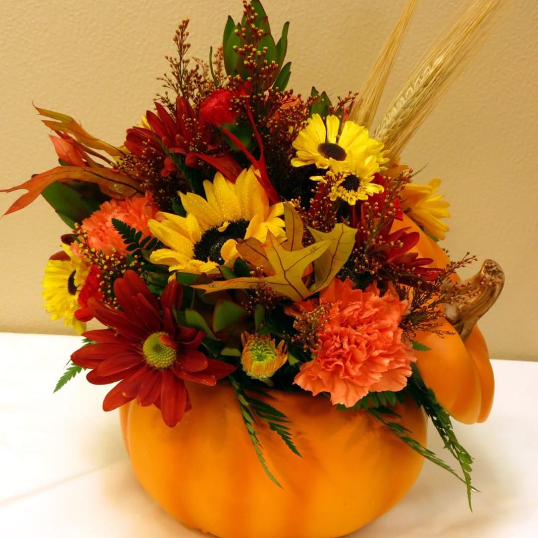 Fall floral arrangement in a pumpkin container with sunflowers and daisies